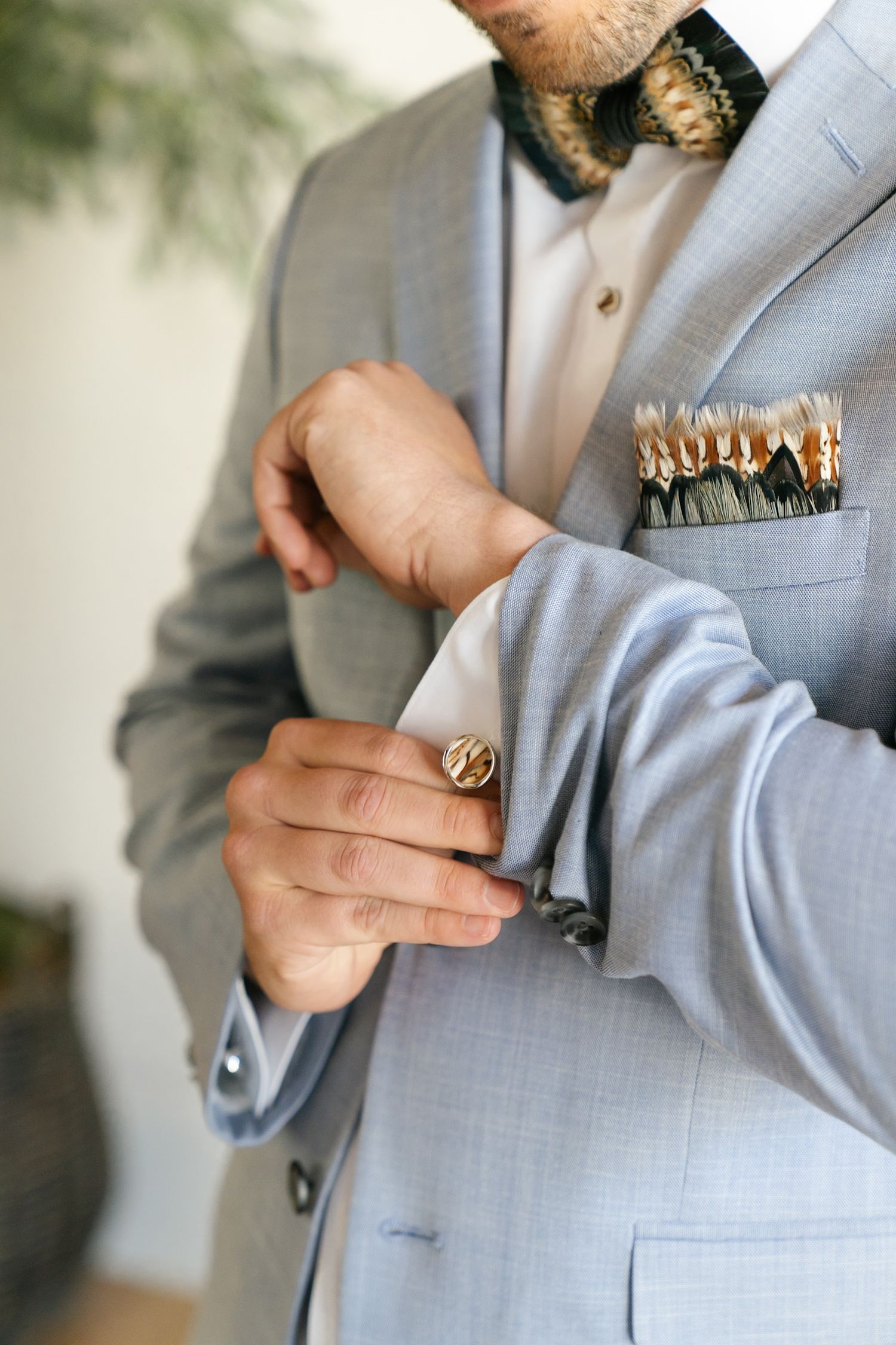Close up of hands adjusting cufflink on light gray suit with floral boutonniere and pocket square details.