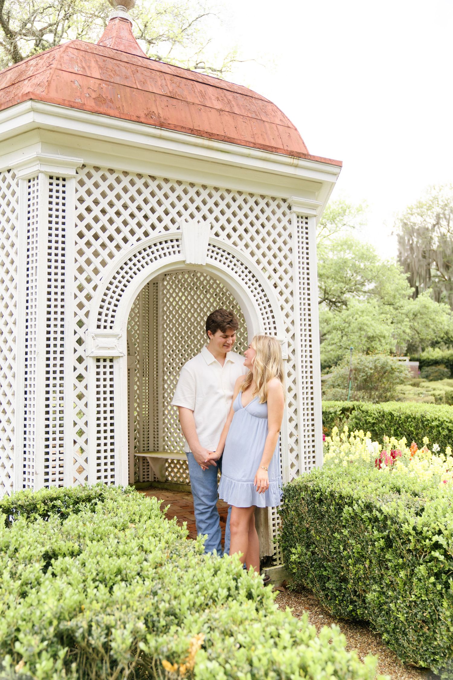 Couple posing together by decorative white gazebo with lattice details.