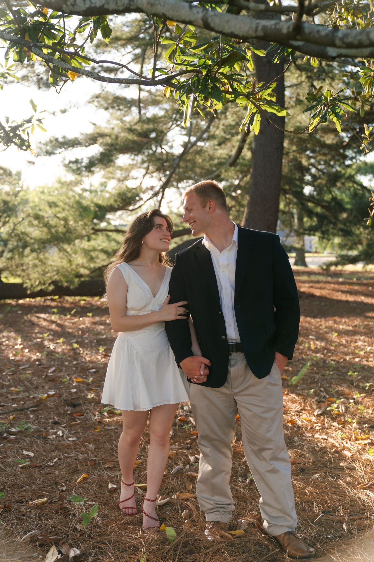 Couple walking together on fallen autumn leaves in a sunlit wooded area at golden hour.