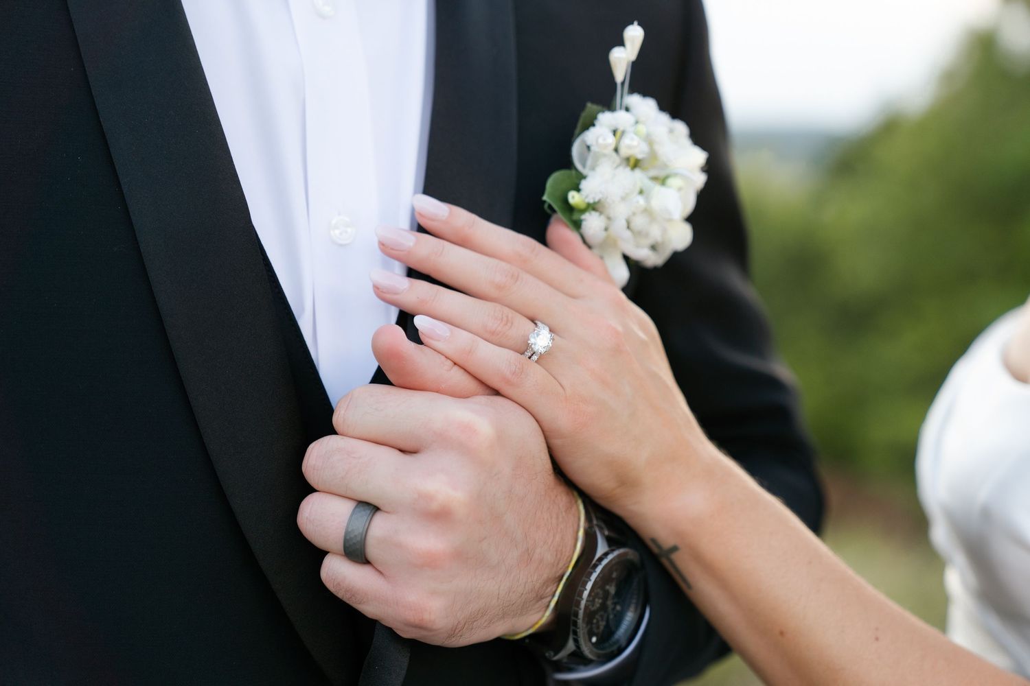Close-up of newlywed couple's hands showing wedding rings and white floral bouquet details.
