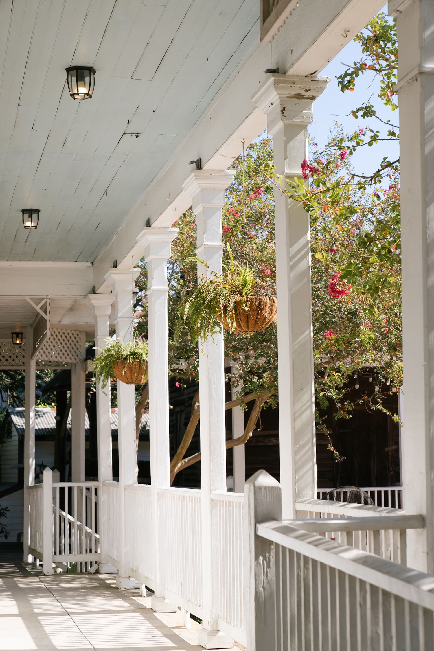 White wooden porch with columns features hanging lanterns and climbing roses creating romantic ambiance.