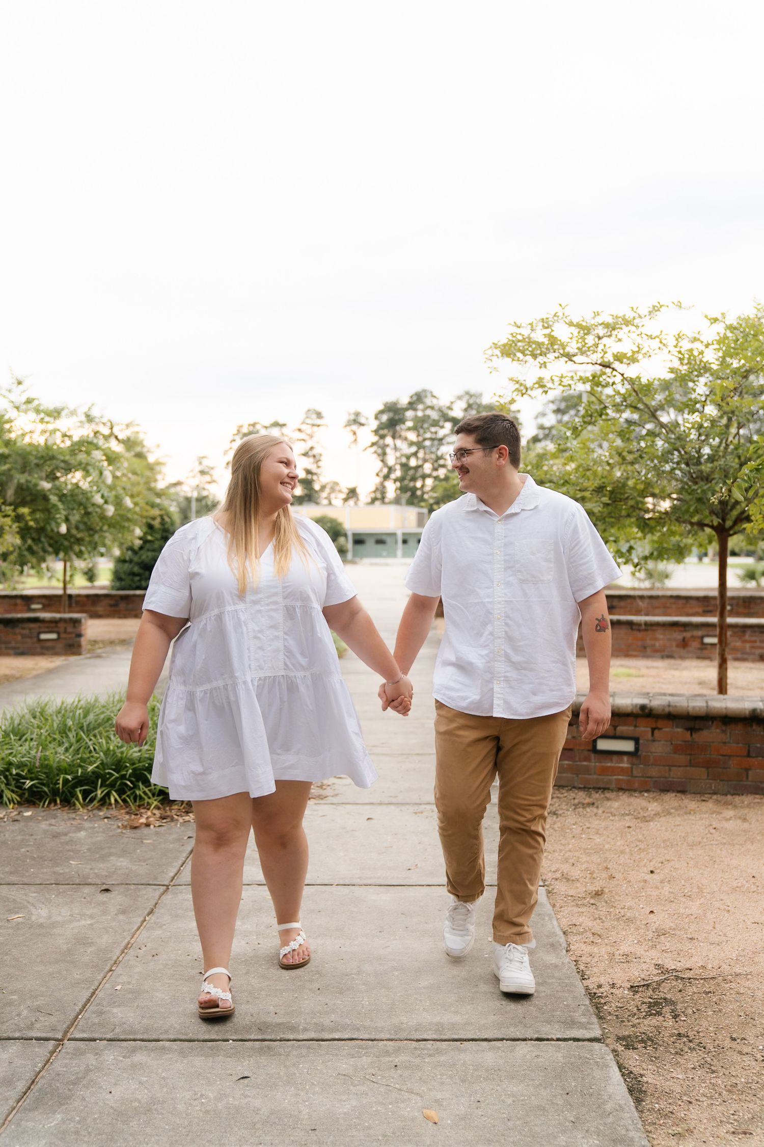 Couple in matching white outfits walking hand in hand on outdoor path.
