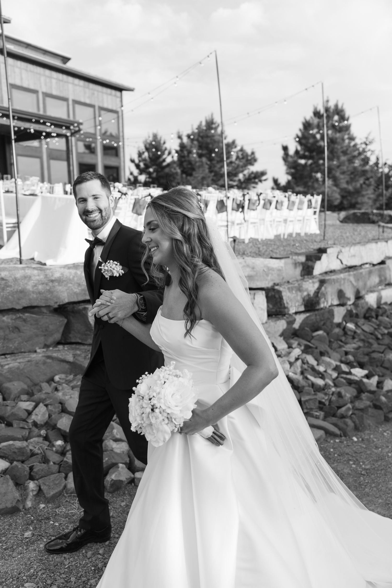 A playful wedding couple shares a candid moment together on a hillside with stone retaining walls.