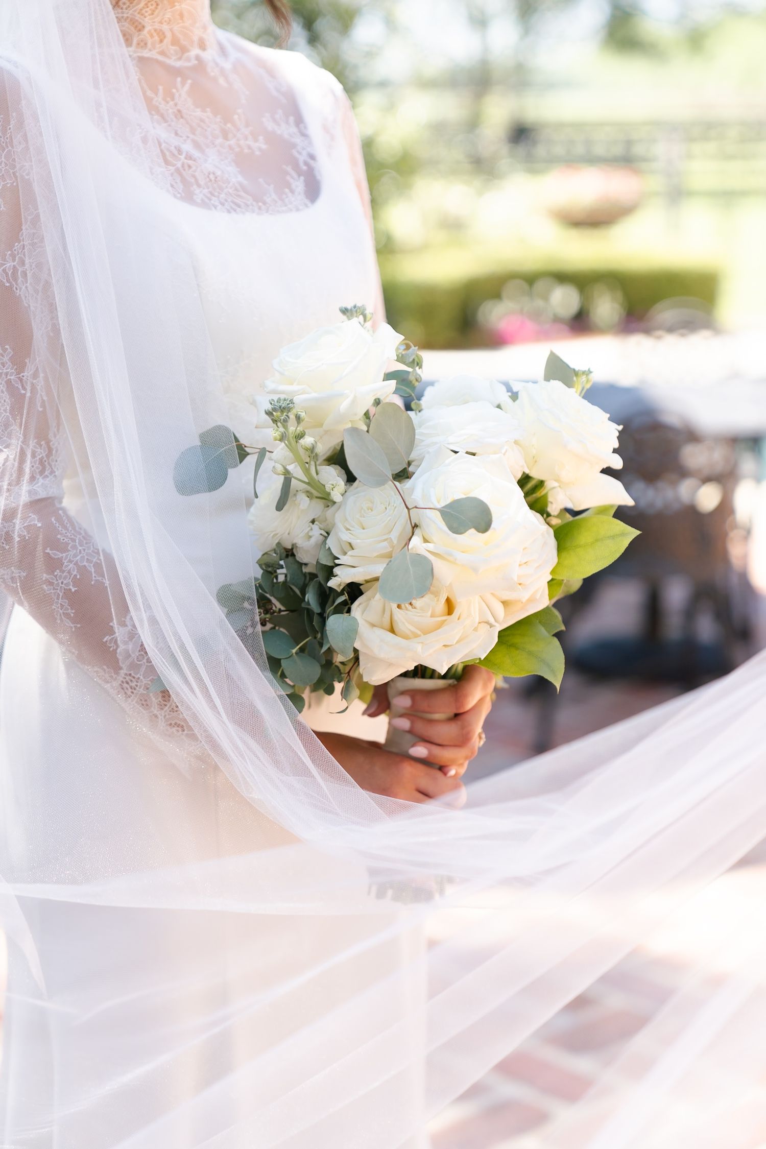 White wedding bouquet with roses and eucalyptus leaves caught in flowing bridal veil.