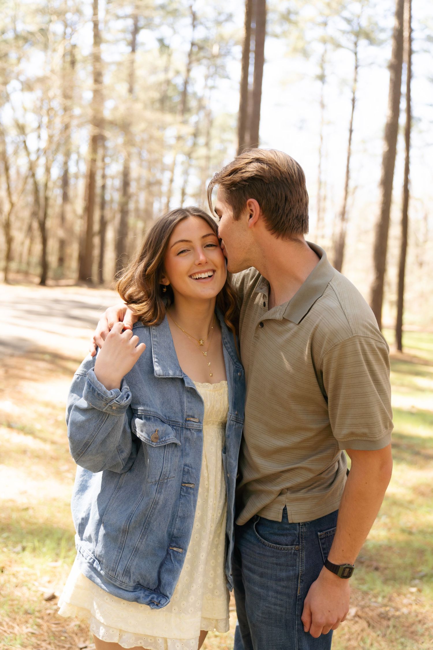 Couple in casual attire sharing playful moments in wooded outdoor setting.