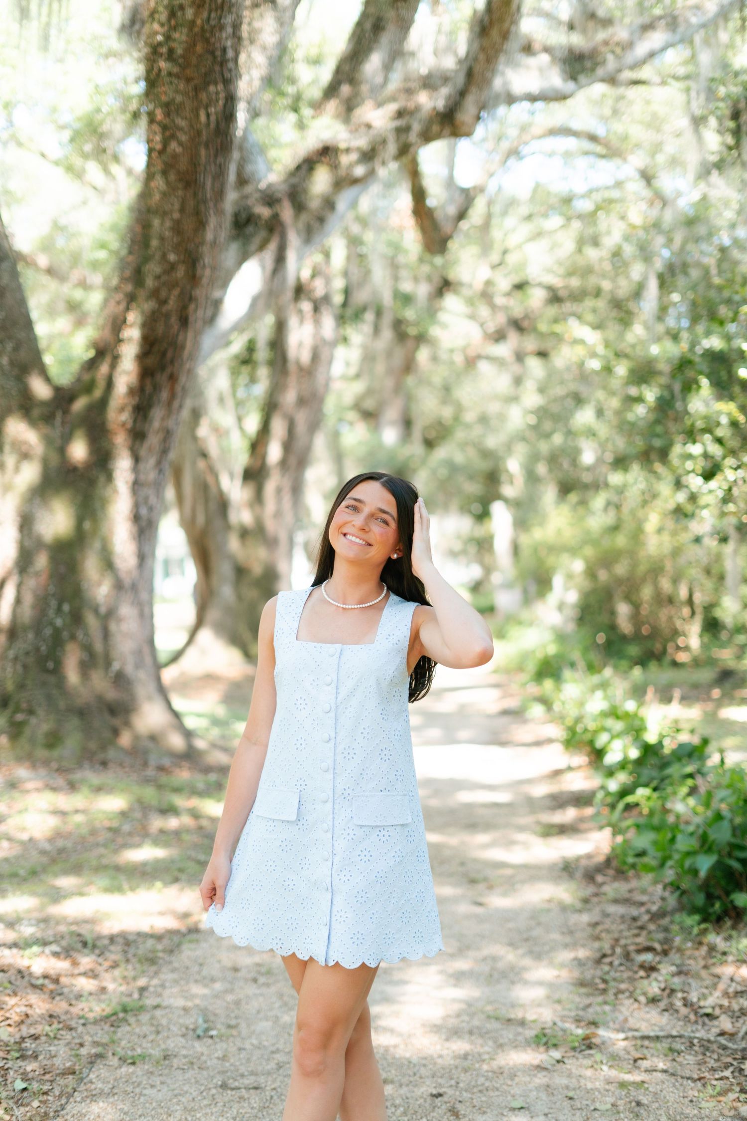 Person wearing light blue dress smiles joyfully while posing in a wooded outdoor setting.