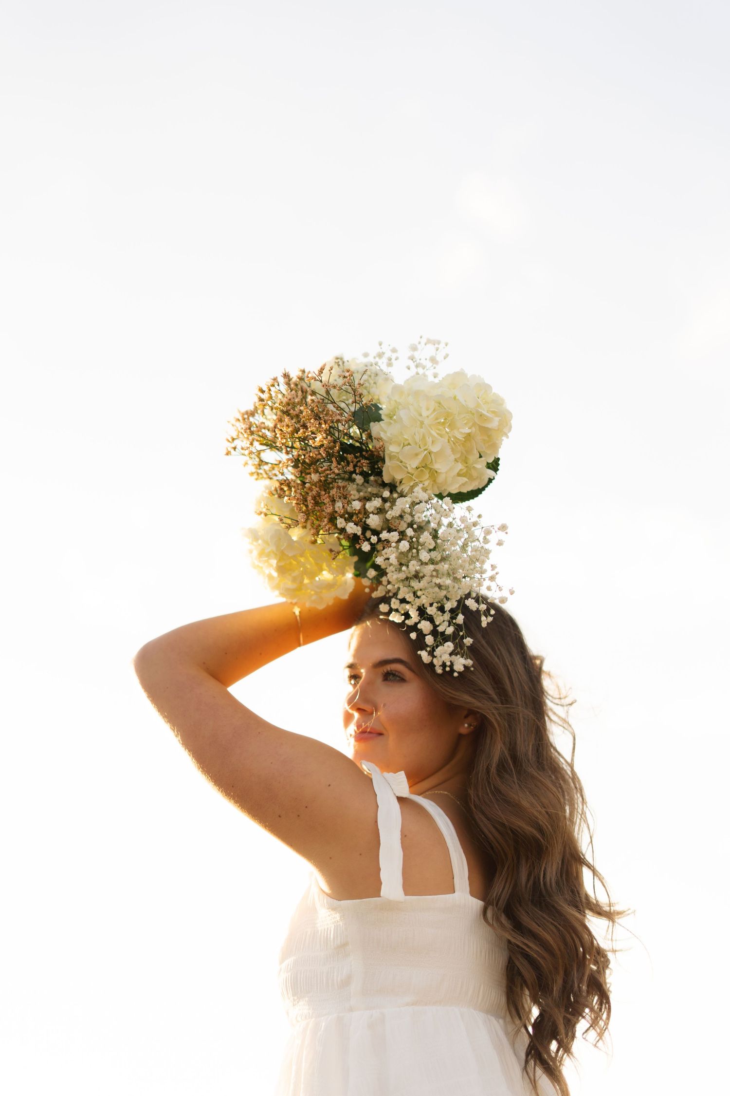Person wearing white dress and baby's breath flower crown posed against bright sunlit background.