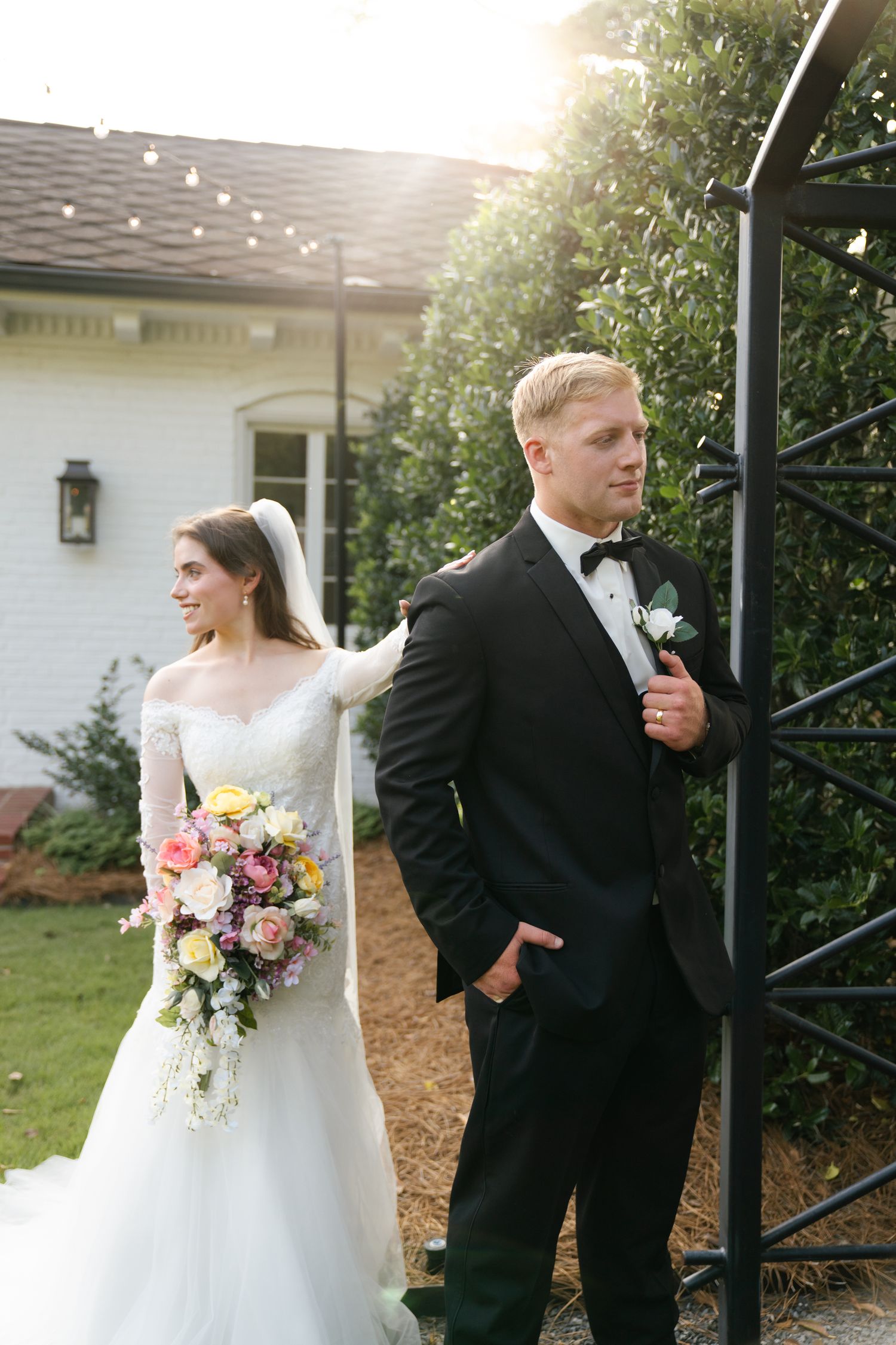 Wedding couple having a playful moment outside in formal attire with lush greenery.