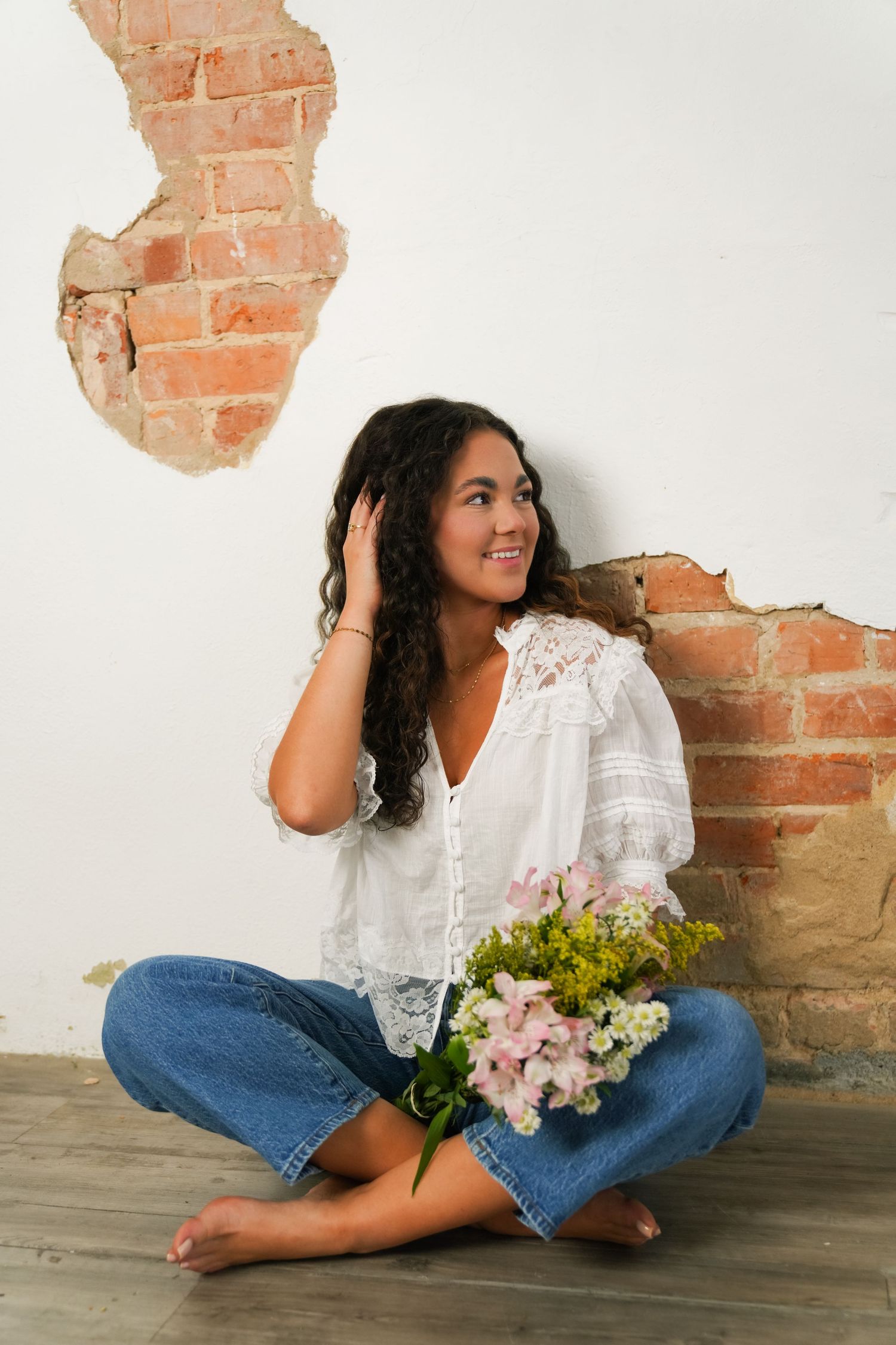 Indoor portrait session against exposed brick wall with floral bouquet and white lace top.