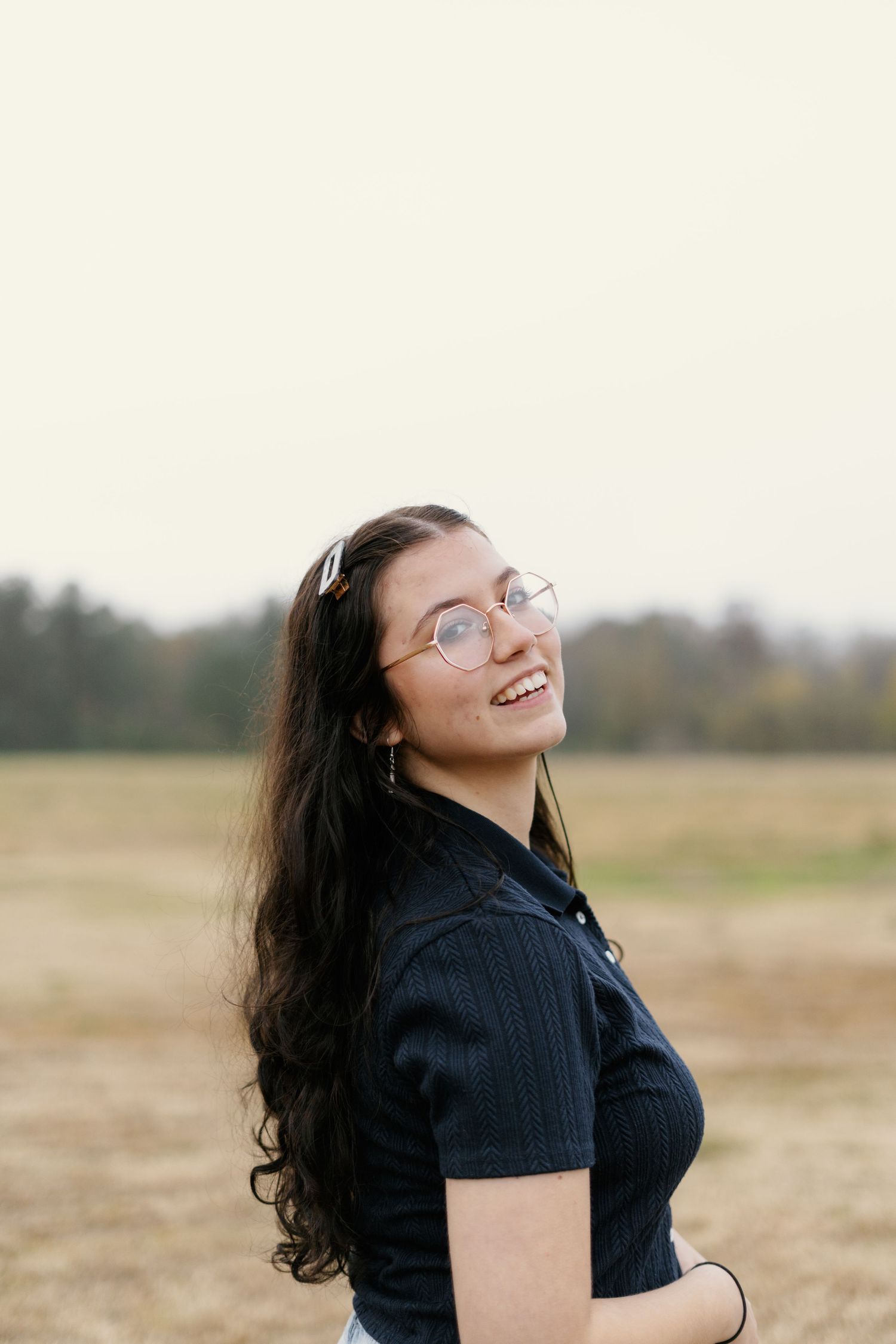 A person in a black shirt laughs joyfully while standing in a field on an overcast day.