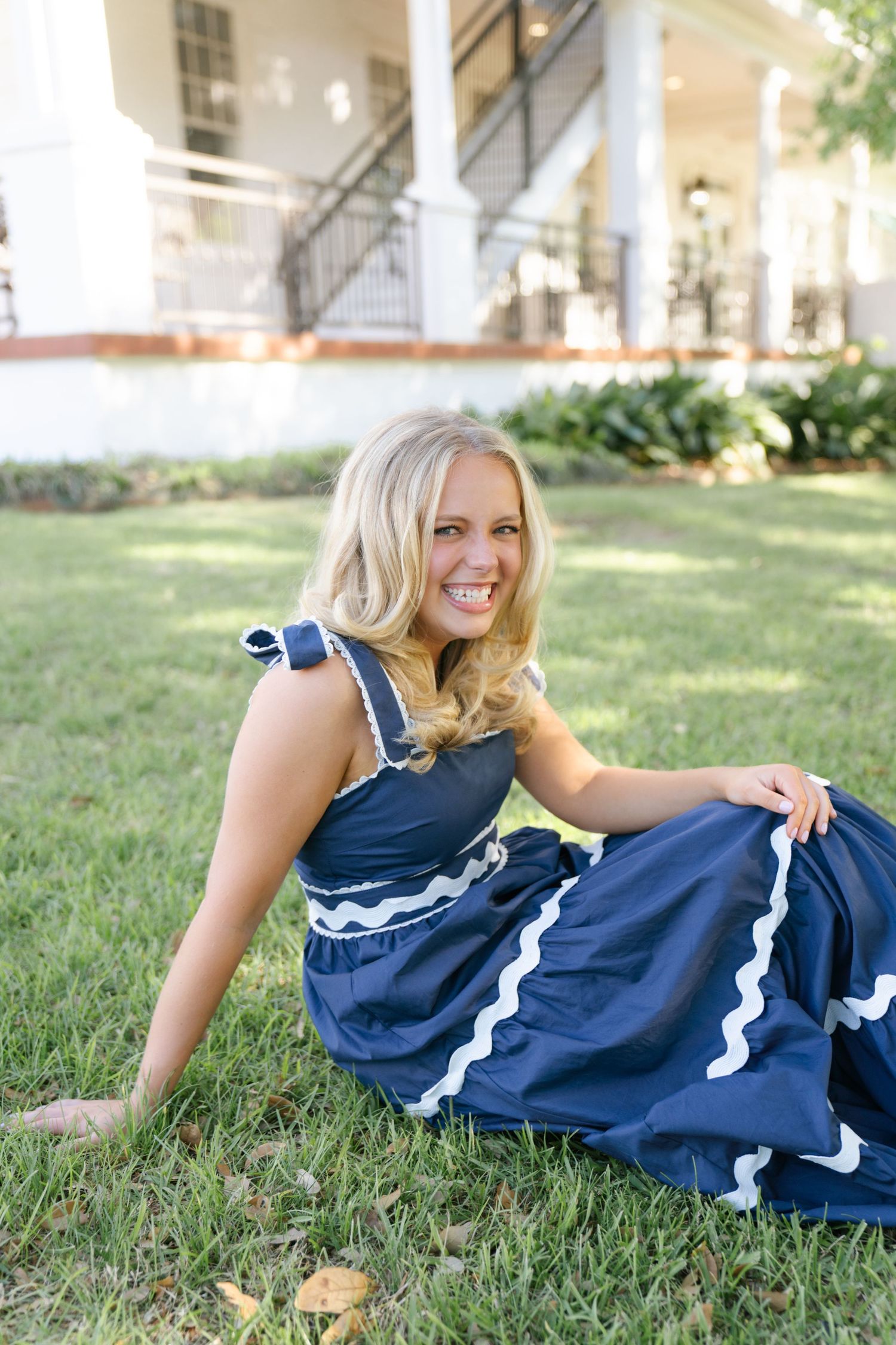 A person in a navy blue and white dress lies casually on green grass in a sunny outdoor setting.