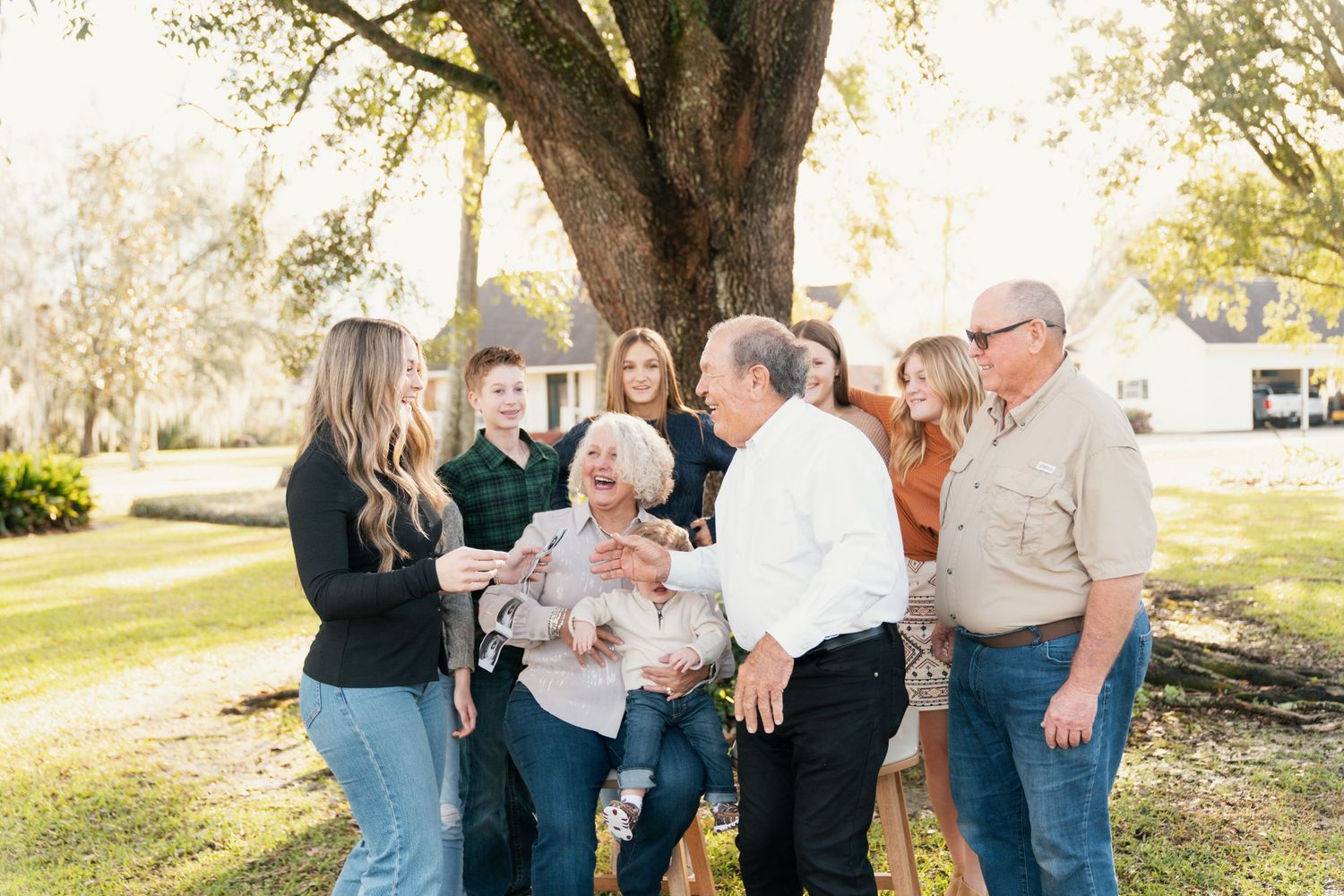 Multi-generational family gathering outdoors under a large tree.