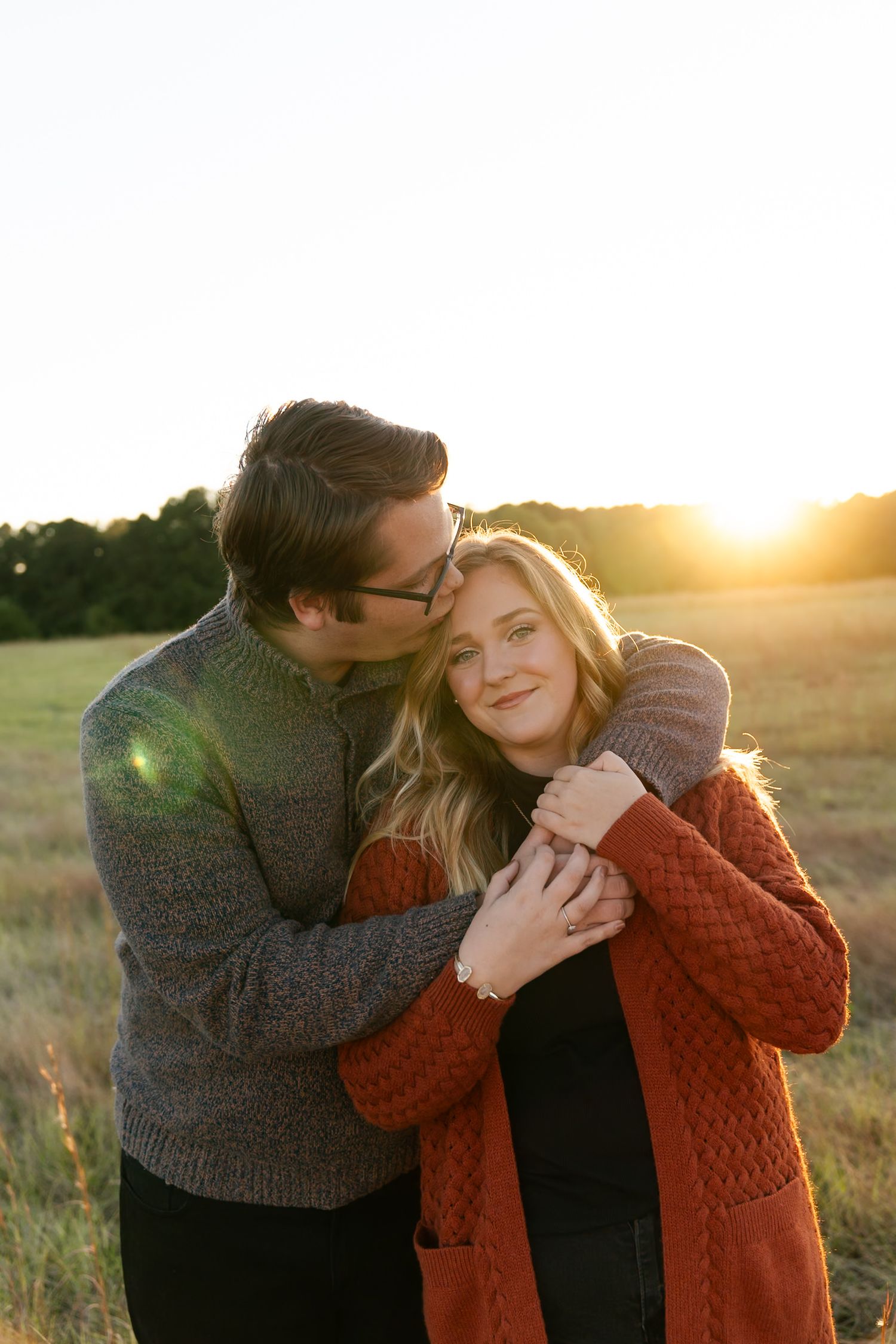 A couple shares an intimate moment in a field at sunset with golden light streaming through their silhouettes.