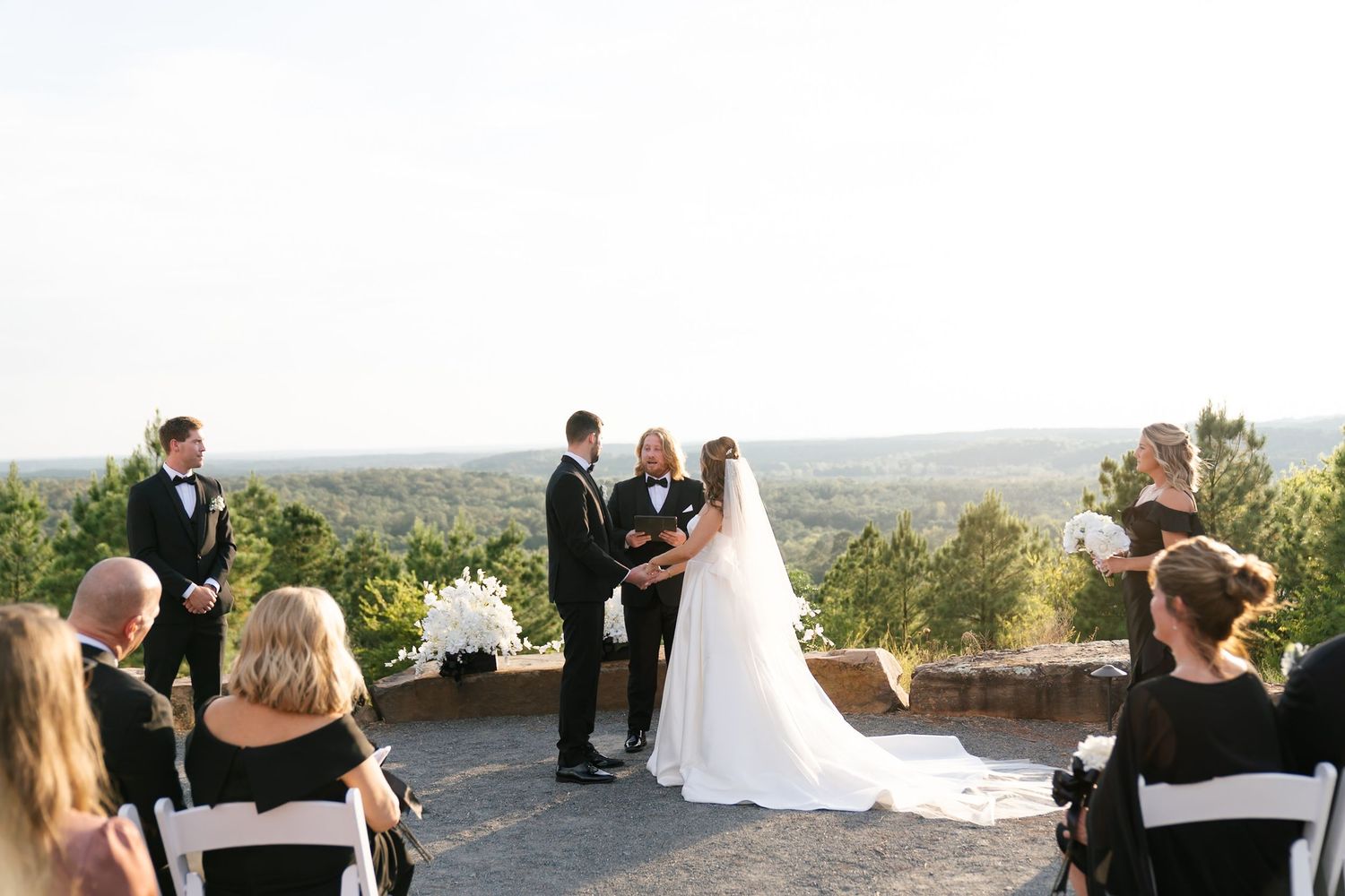 Wedding ceremony guests seated in white chairs on an outdoor terrace overlooking a scenic mountain landscape.