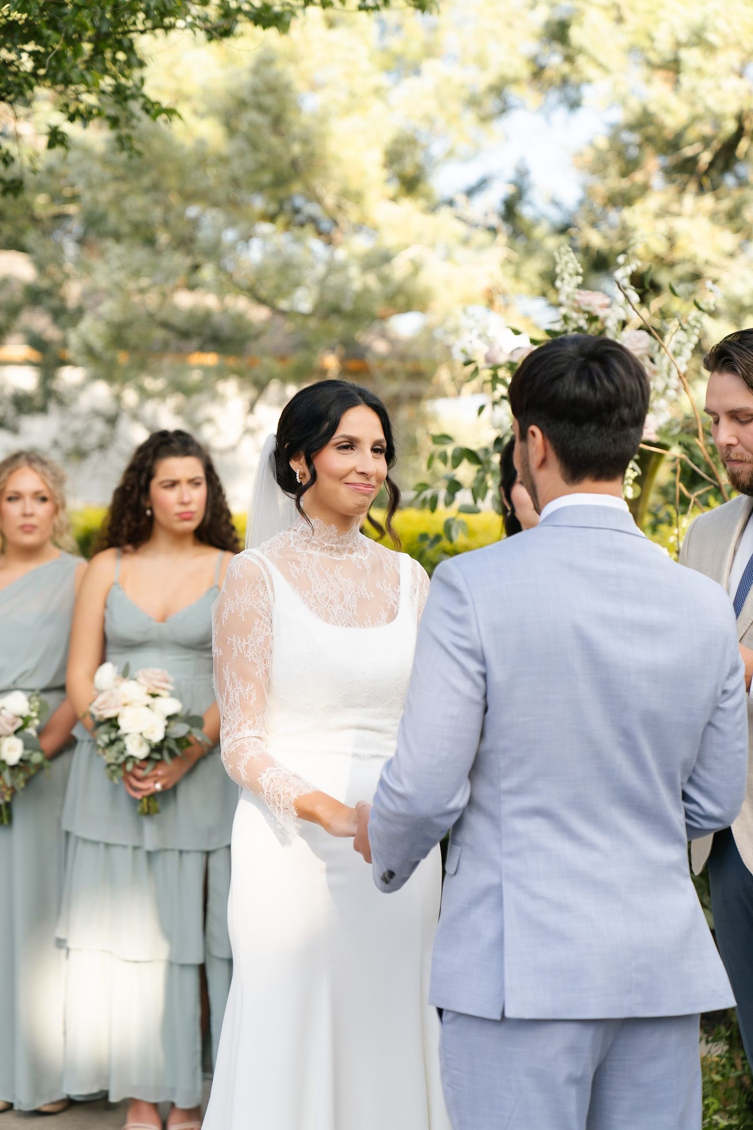Wedding party poses for photos outdoors in coordinating gray and sage green attire.