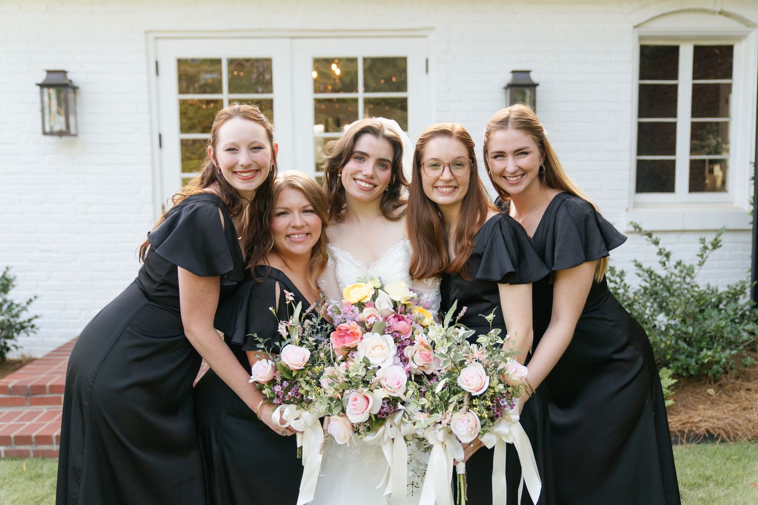 Bridal party in black and white dresses gathered for photos outside white building.