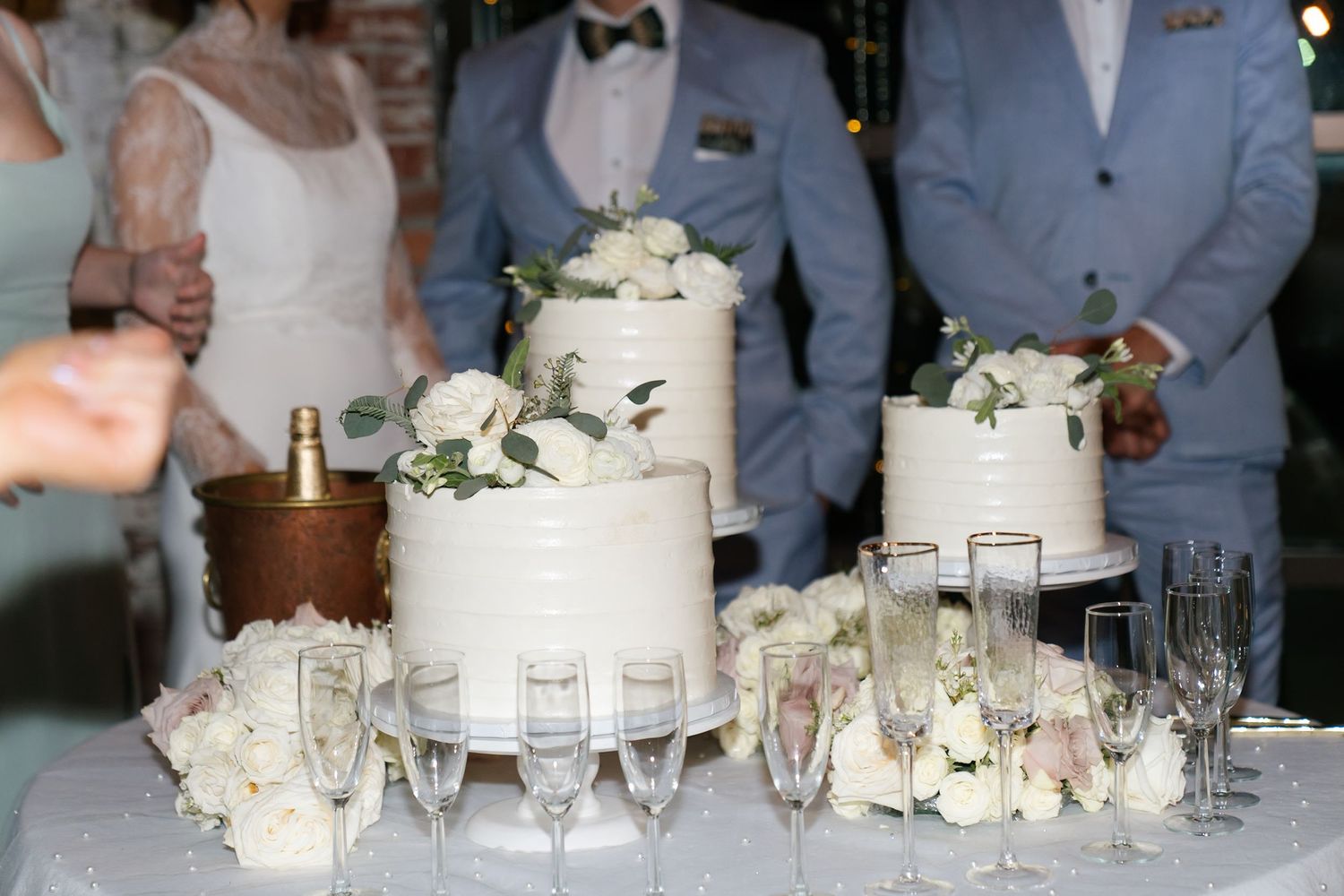 Elegant white wedding cake display with rose decorations and champagne glasses.