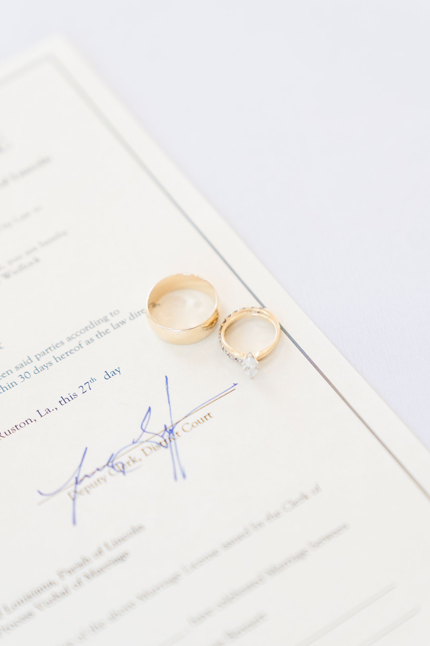 Two gold wedding rings rest on signed marriage documents with blue ink signatures.