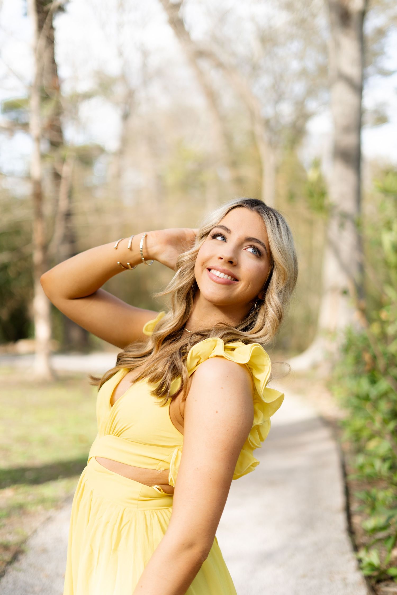 Figure in yellow dress poses joyfully in outdoor garden setting on sunny day.