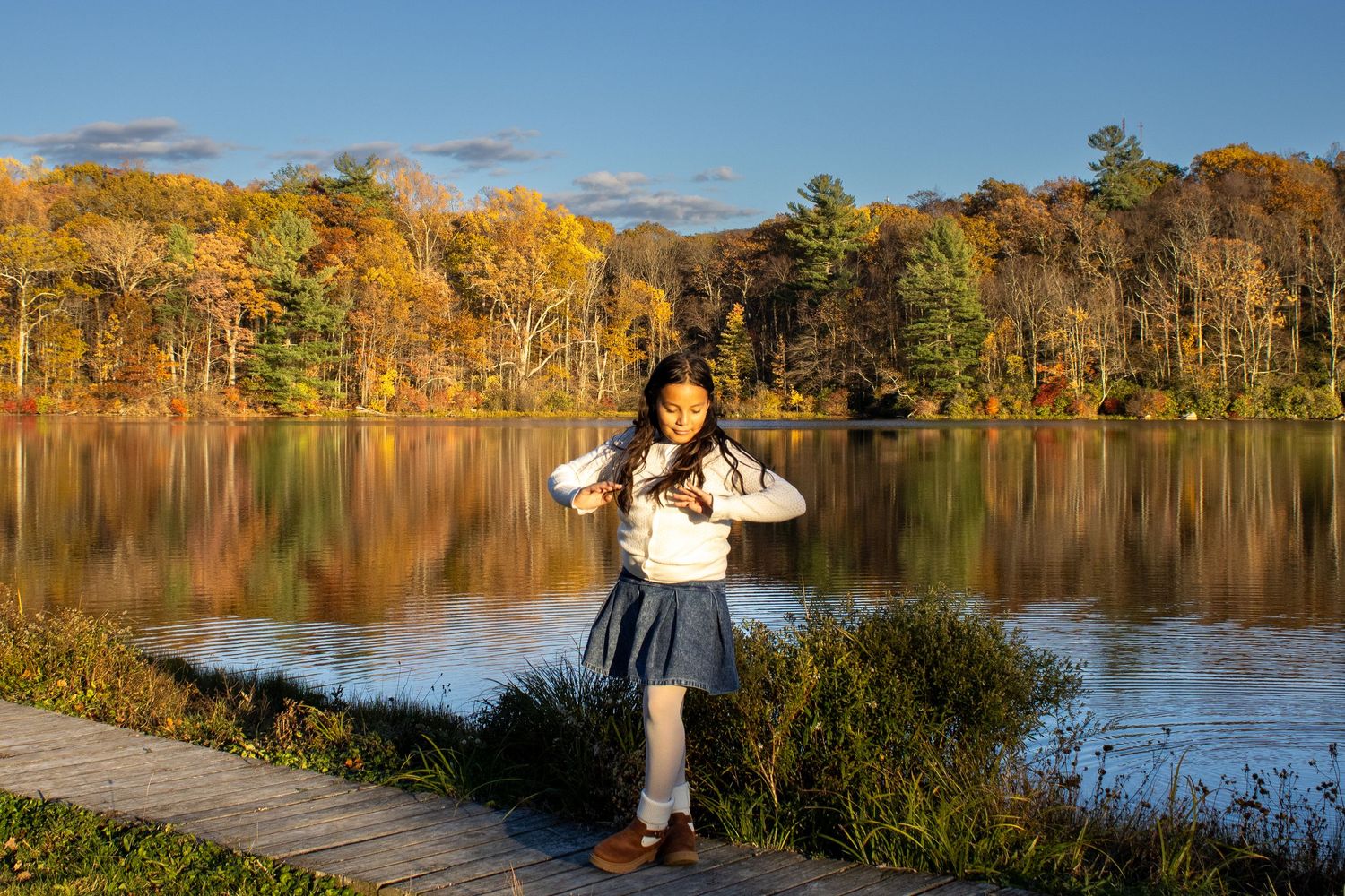 Person posing by scenic autumn lake with colorful fall foliage reflecting in water.