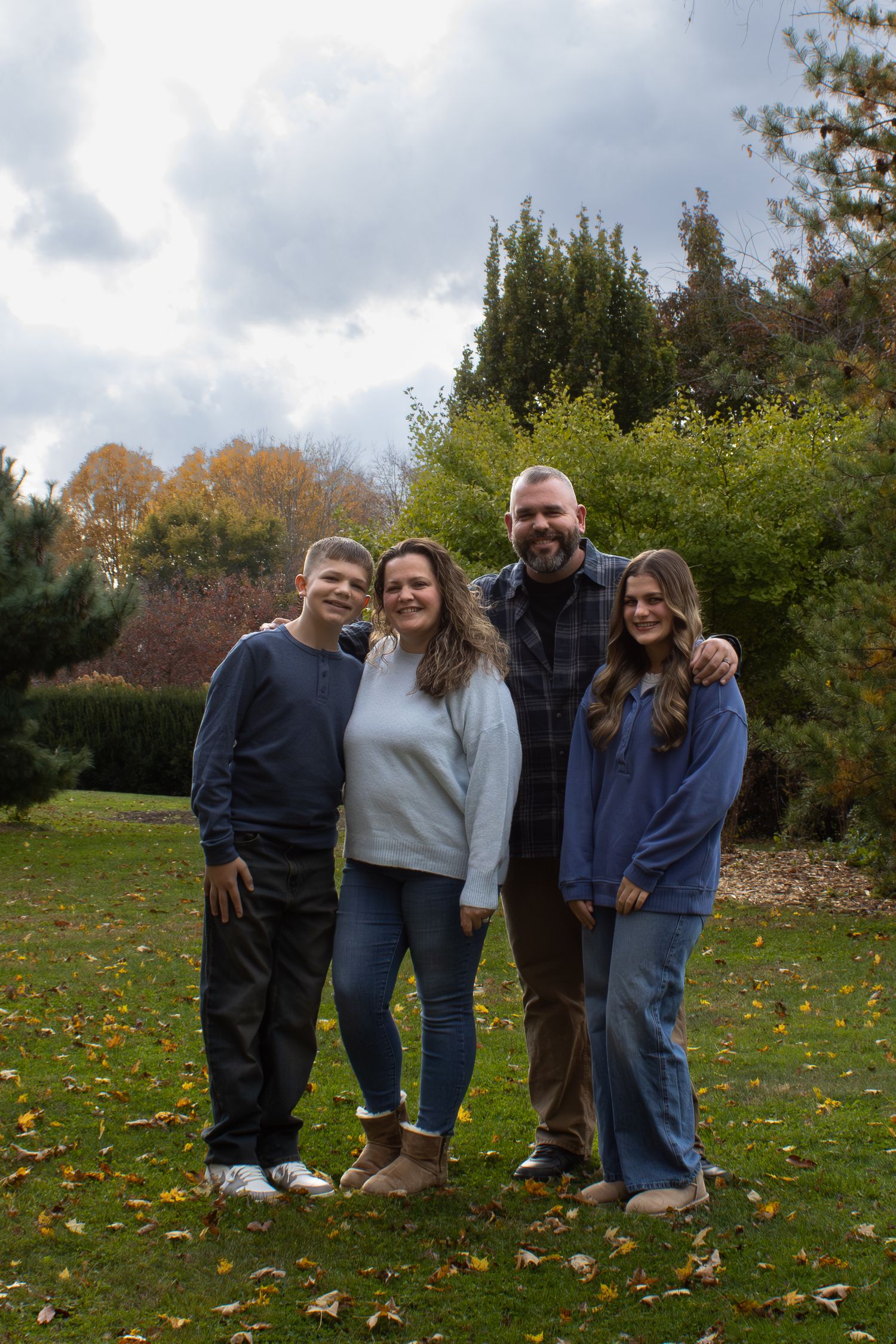 Family of four poses together outdoors during fall with autumn foliage in the background.