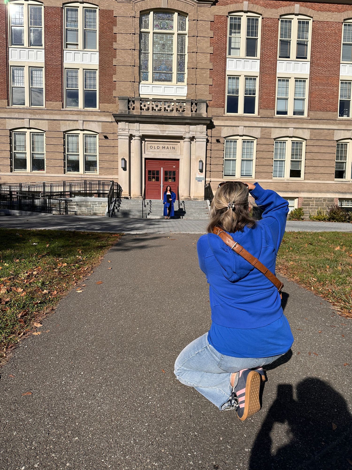 Person in blue hoodie sitting on steps in front of brick building.