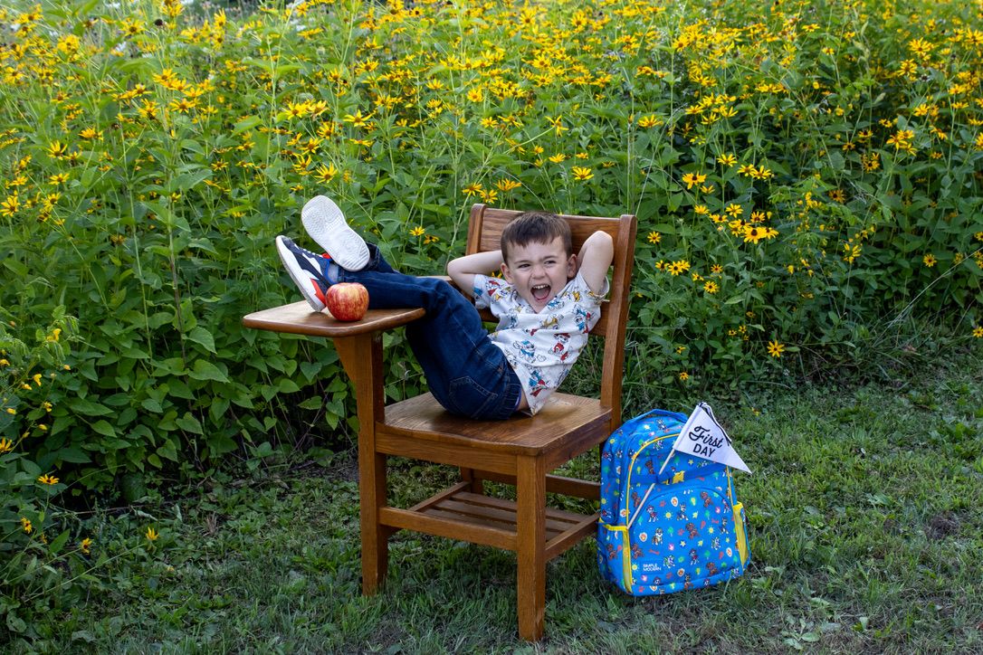 Wooden chair with school supplies and backpack in field of yellow wildflowers.