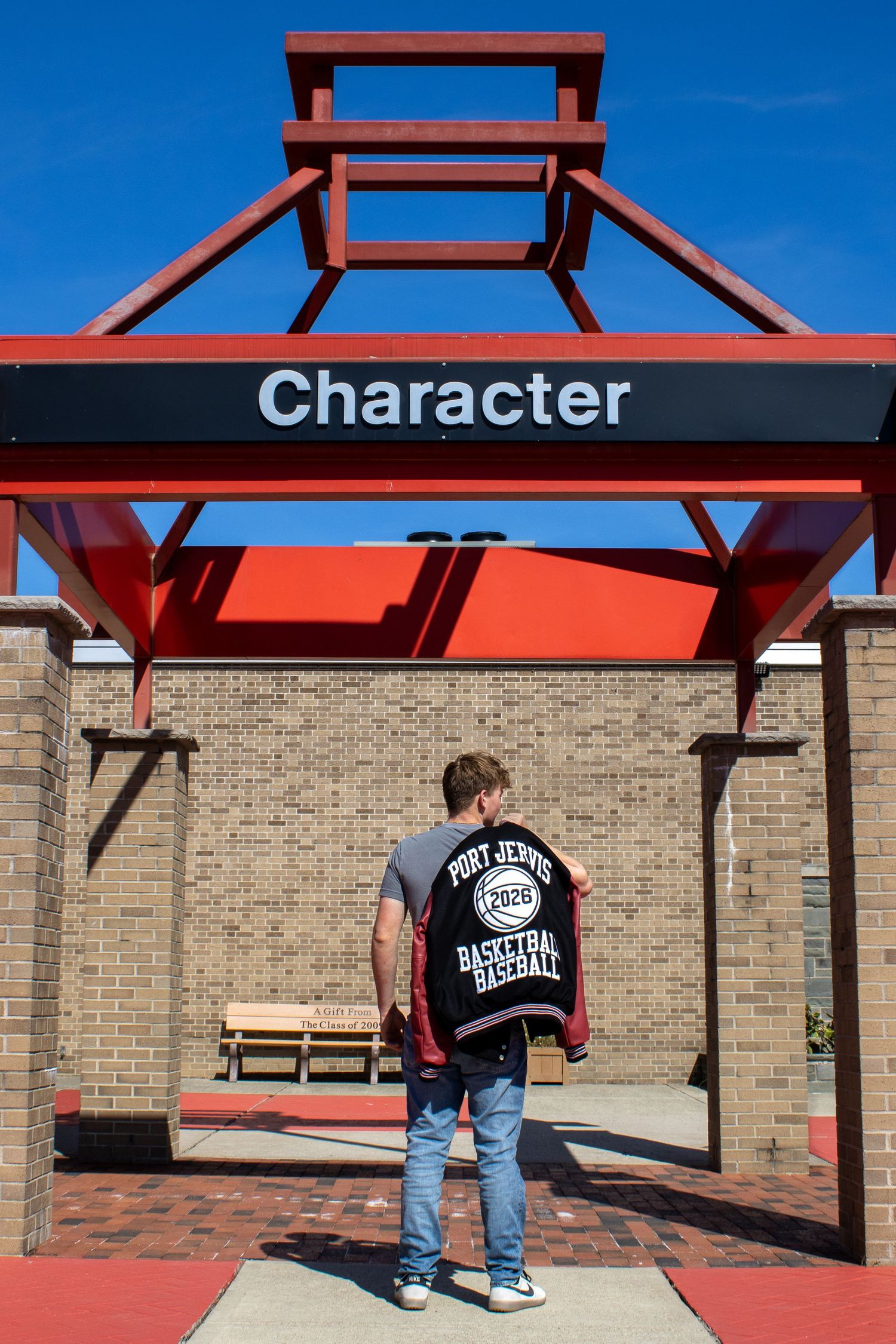 Student stands under red 'Character' sign wearing varsity jacket at school entrance.