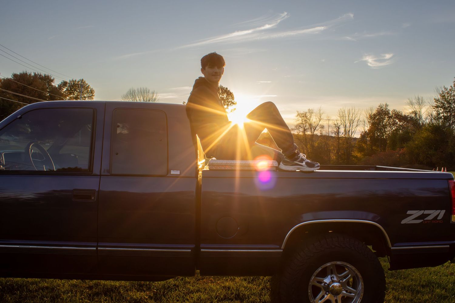 Silhouette of a pickup truck against a vibrant sunset with lens flare.