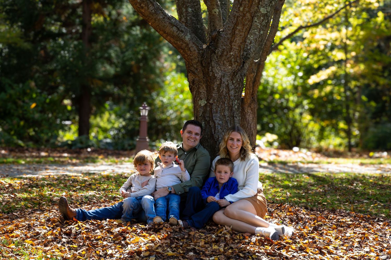 Family gathering under large tree with autumn leaves scattered on ground.