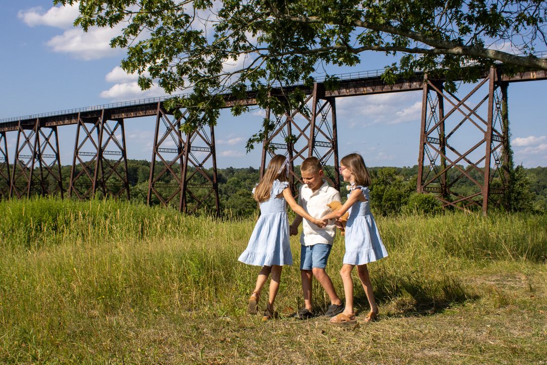Two ten year old girls and a ten year old boy play ring around the rosy in a clearing at the Moodna Viaduct in Schunnemunk State Park.
