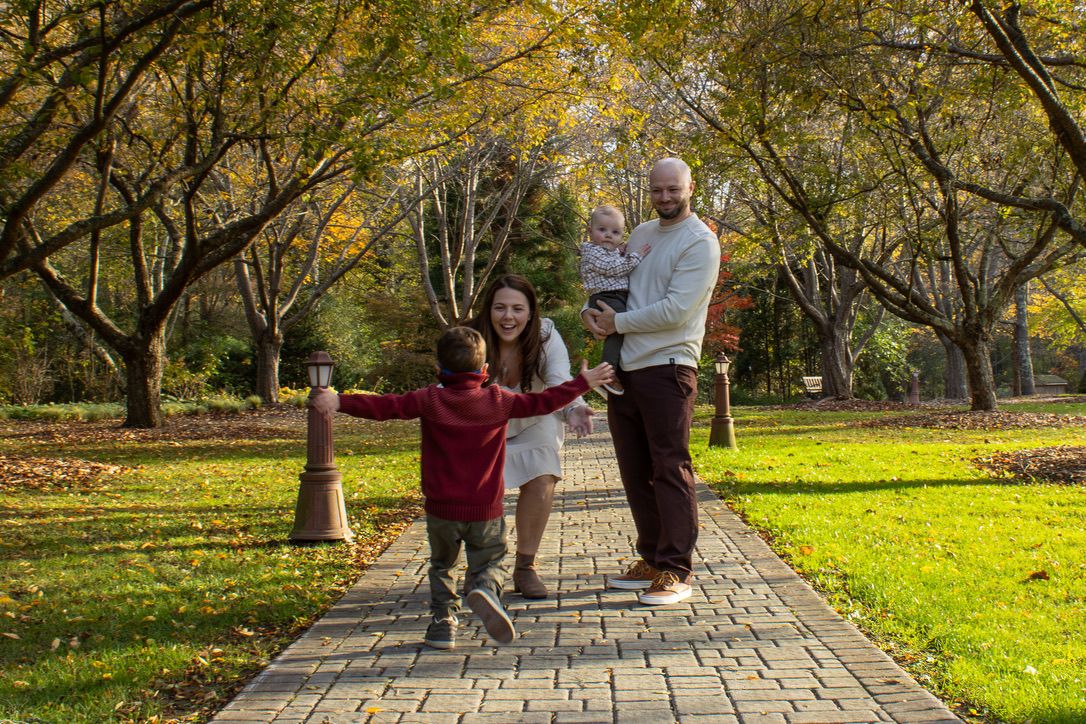 Family walking together on a stone path through a park with golden autumn trees.