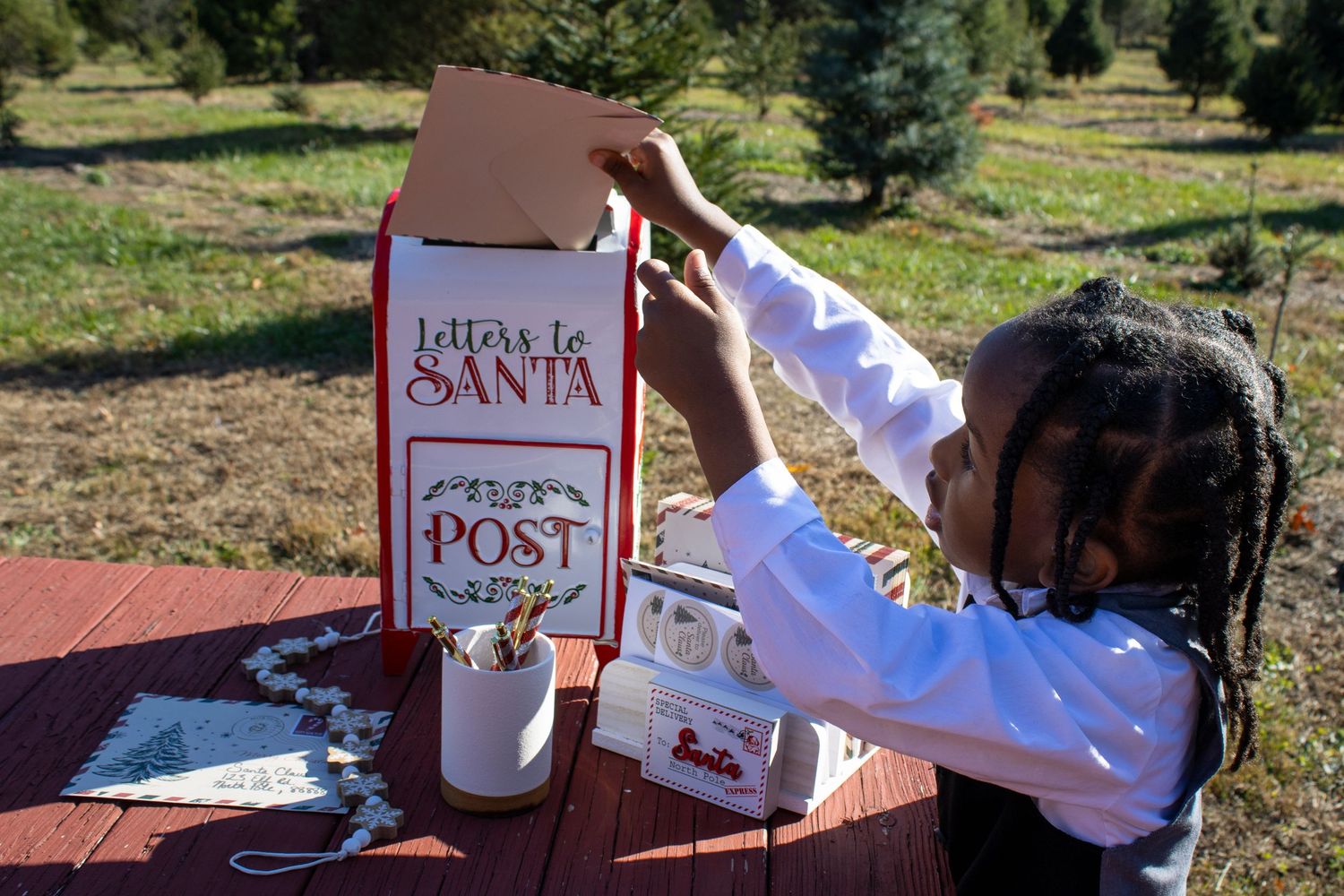 Red wooden picnic table with letters to Santa and holiday decorations in an outdoor setting.