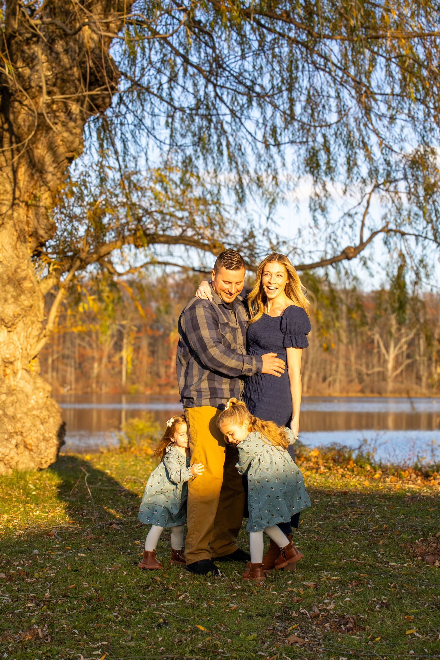 Family enjoying autumn sunset by lake with willow trees in golden light.