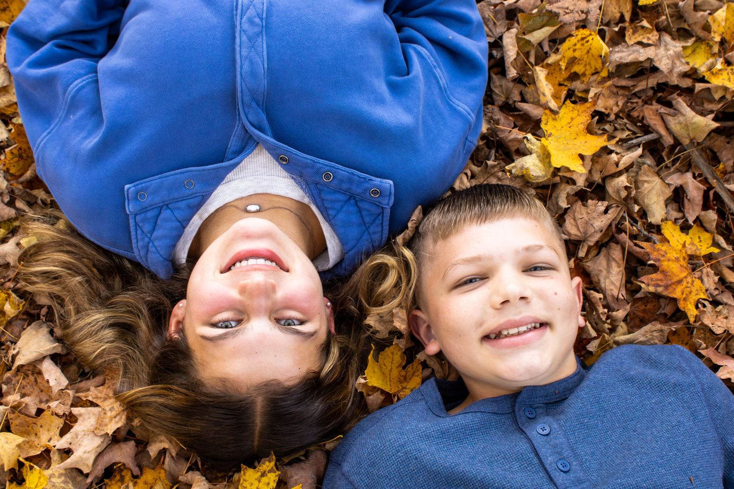Two people lying in fallen autumn leaves wearing blue clothing.
