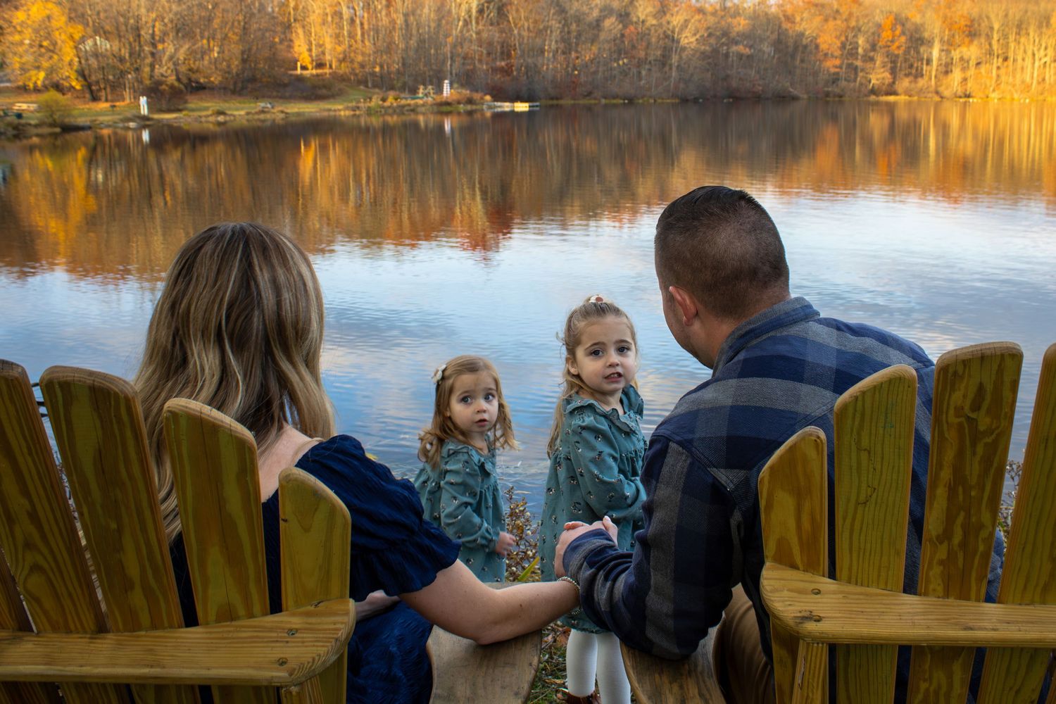 Group seated on wooden bench overlooking lake at sunset.