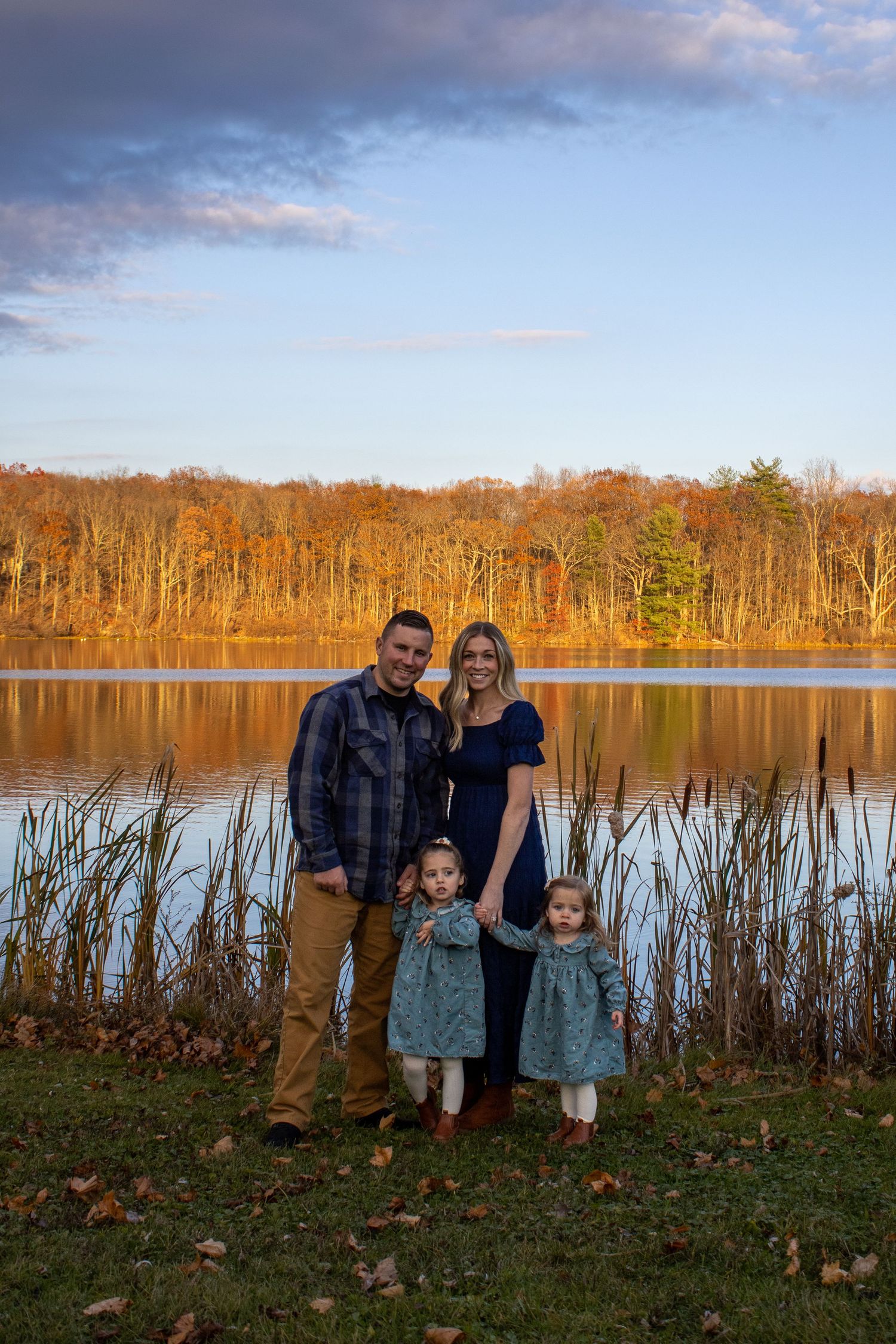 Family gathering at sunset by lake with autumn trees in background.