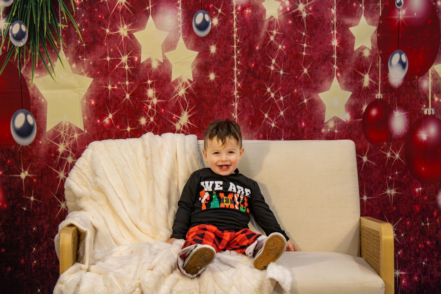 Holiday photo scene with a child on a cream couch against a red backdrop with sparkling stars and ornaments.