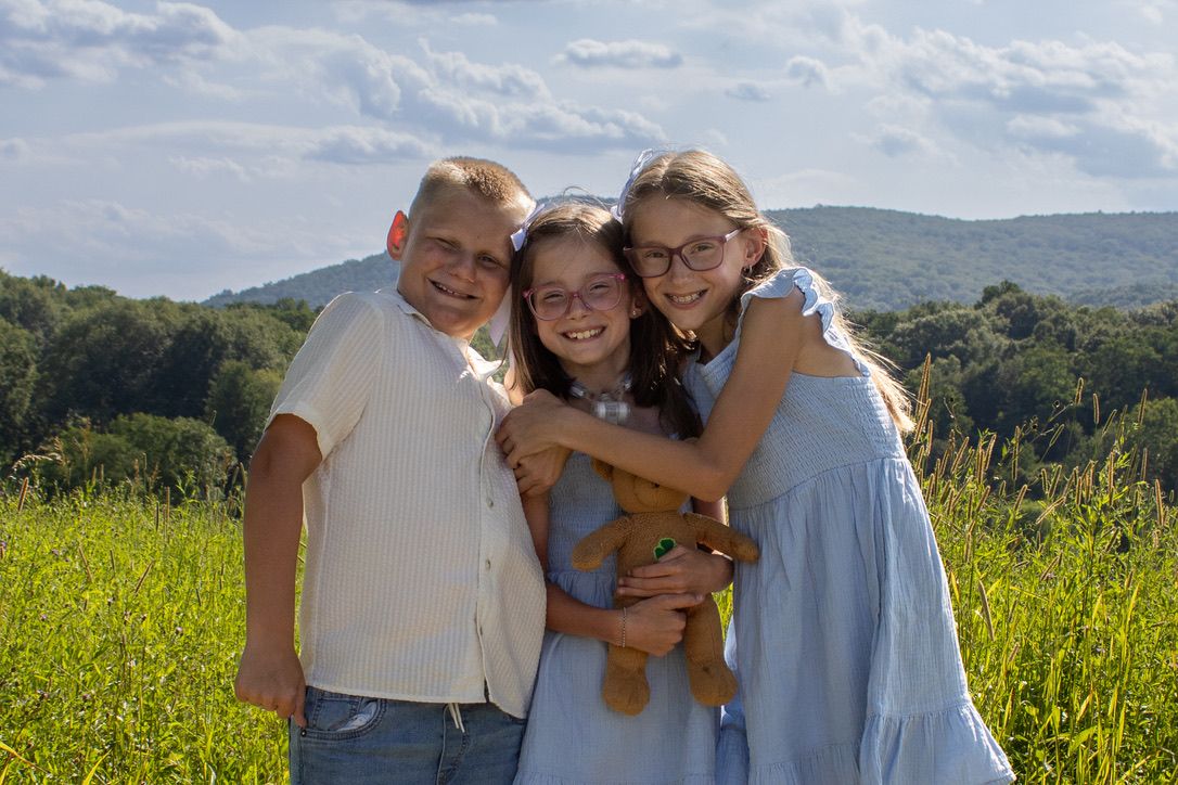 Three siblings share a hug amid the beautiful backdrop of the Schunnemunk Mountains.