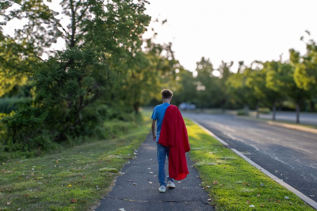 A high school senior walks away down a tree lined path while draping his red graduation gown over his shoulder.