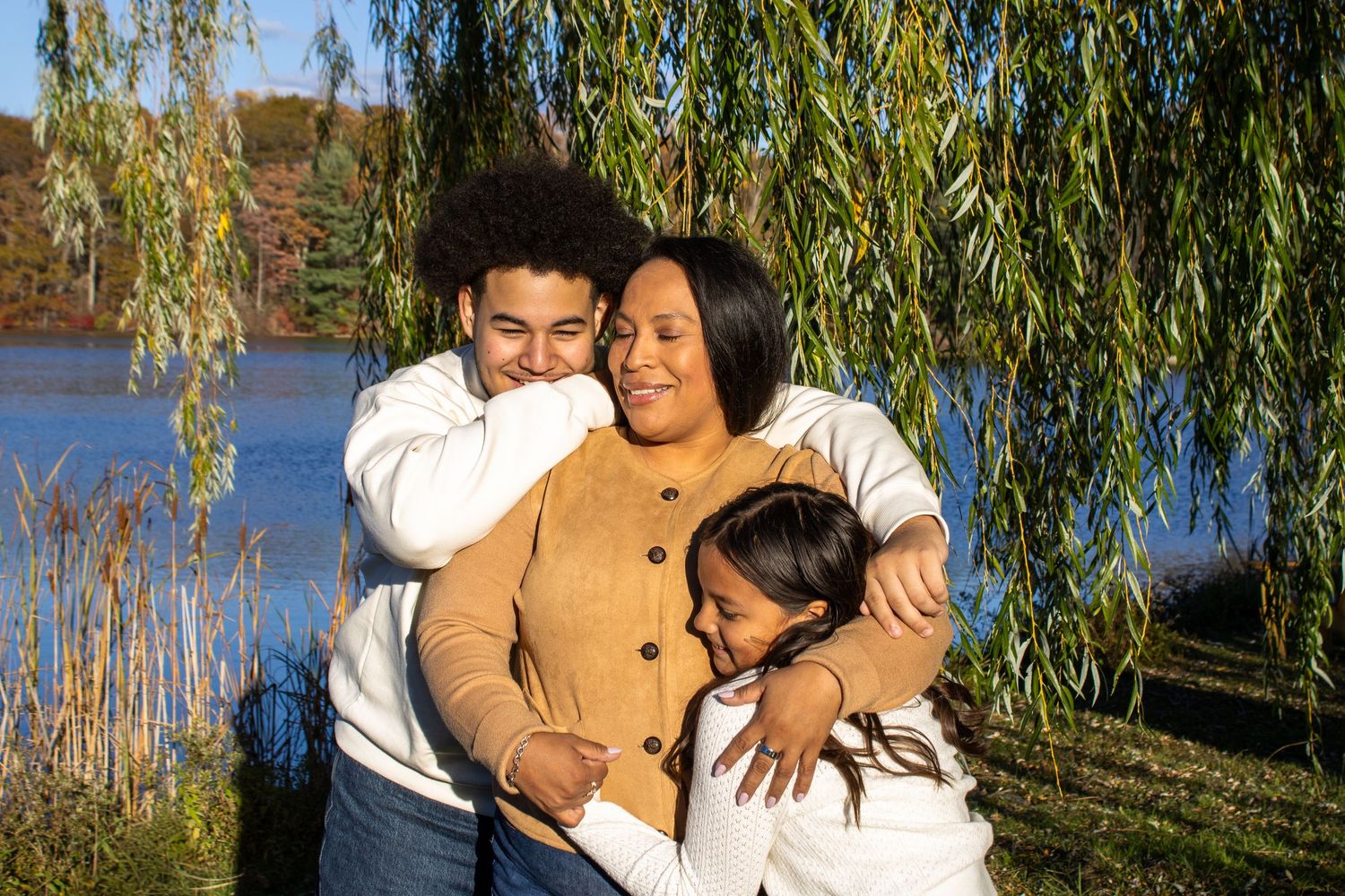 Casual outdoor family portrait against willow tree and water backdrop.