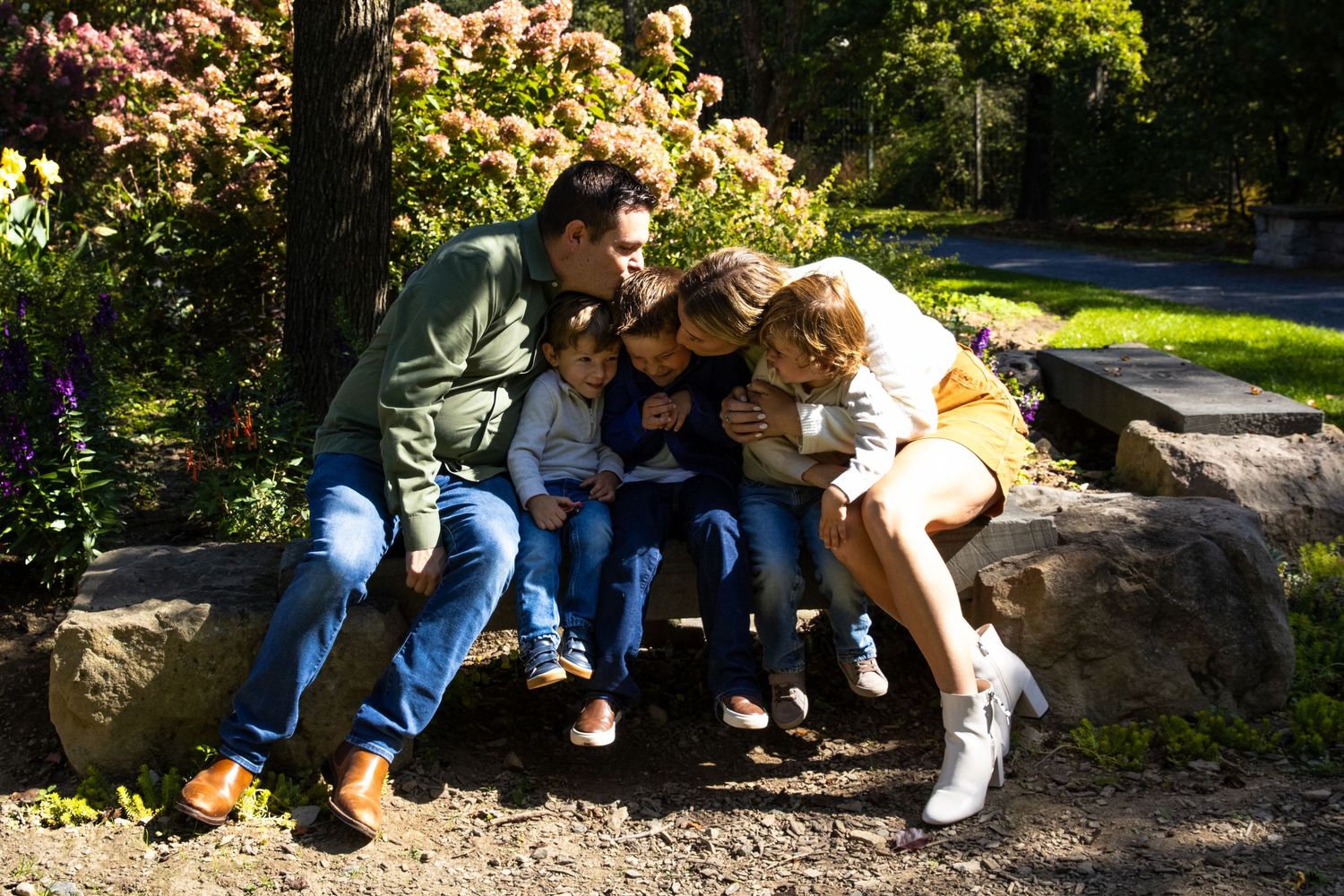 People sitting together on stone wall in dappled sunlight under trees.