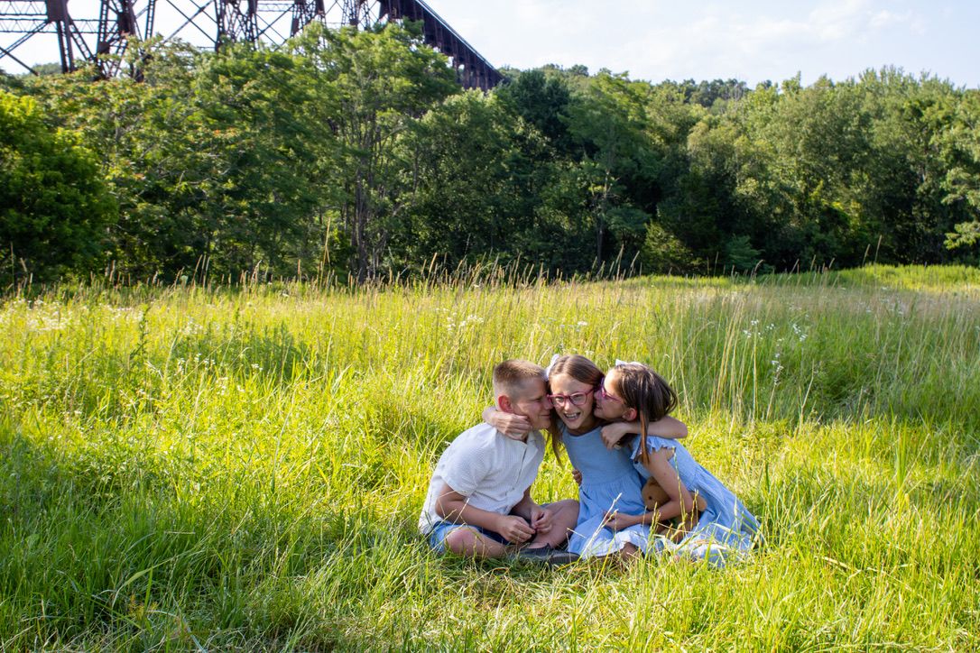 Triplets sit and share a snuggle in a grass field in Salisbury Mills, NY.