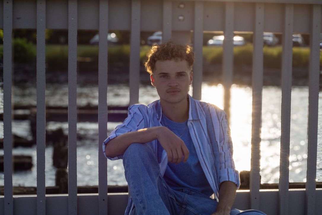 Person in blue shirt leaning against railing during golden hour lighting.