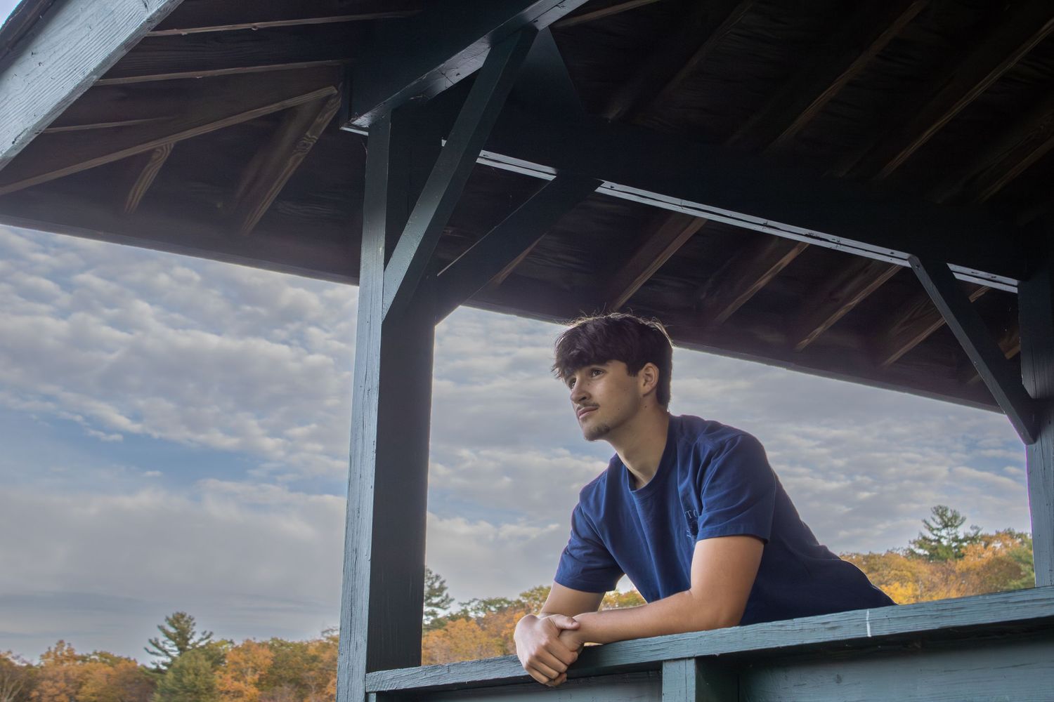 Person sitting under wooden shelter during golden hour overlooking scenic landscape.