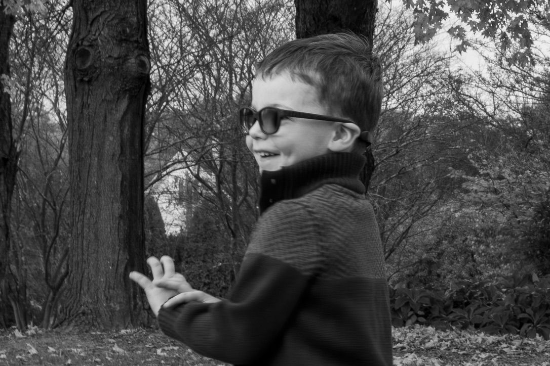 Black and white portrait of a young child in glasses gesturing outdoors.
