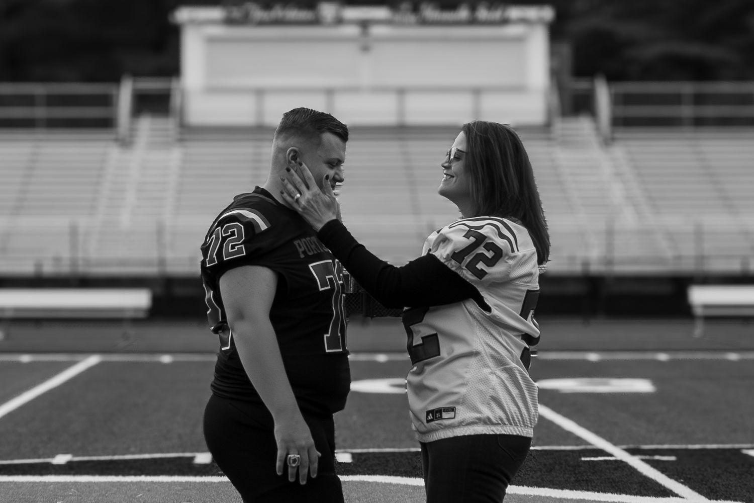 Athletic couple shares tender moment on football field.