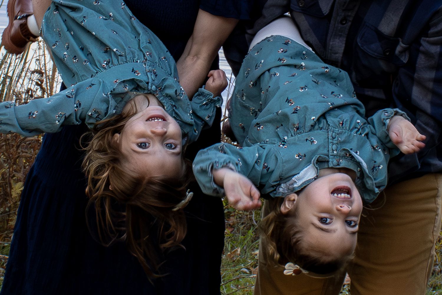 Playful family photo session with children being held upside down outdoors.