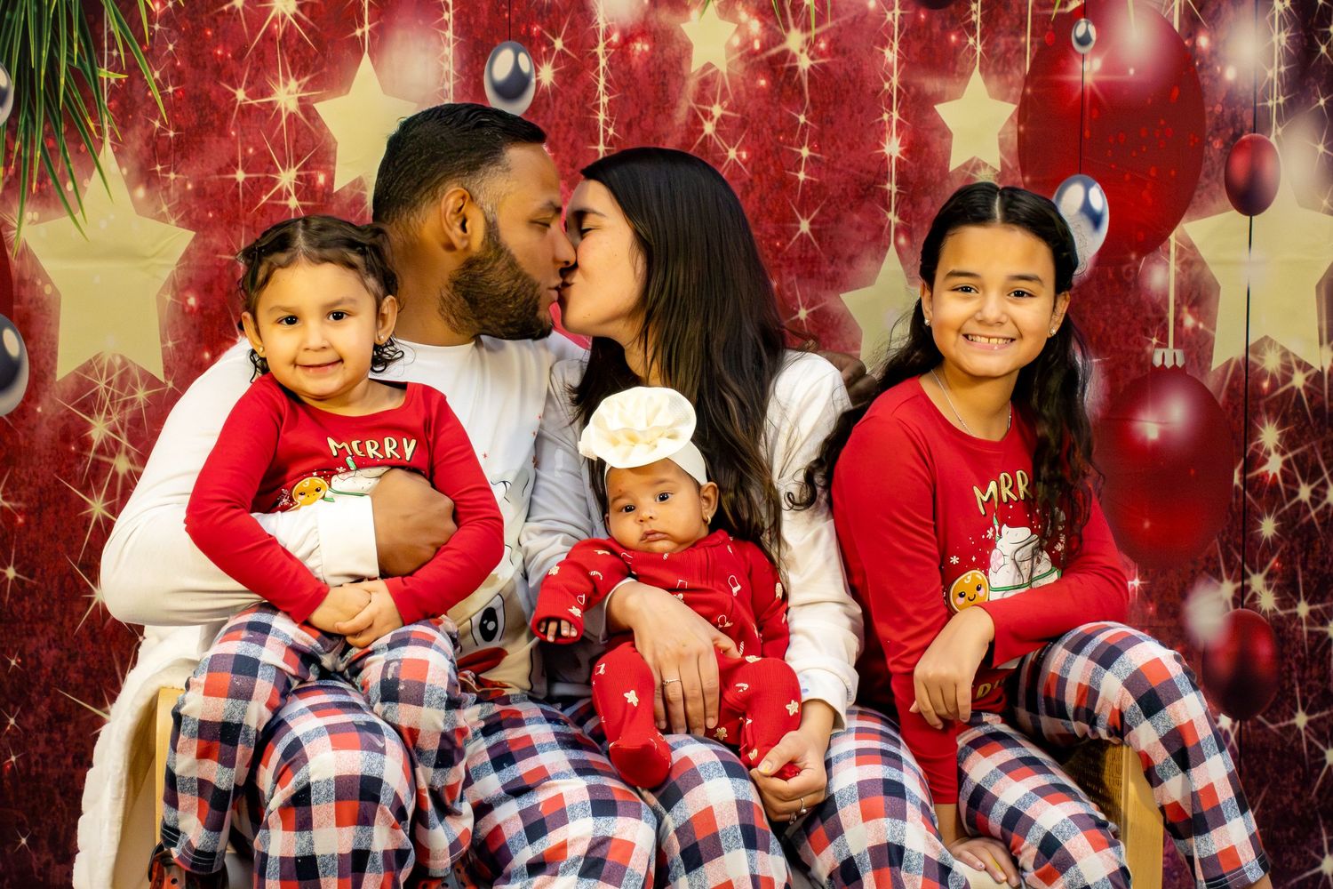 A group wearing coordinated red and plaid outfits poses together for holiday photos with festive sparkly decorations.