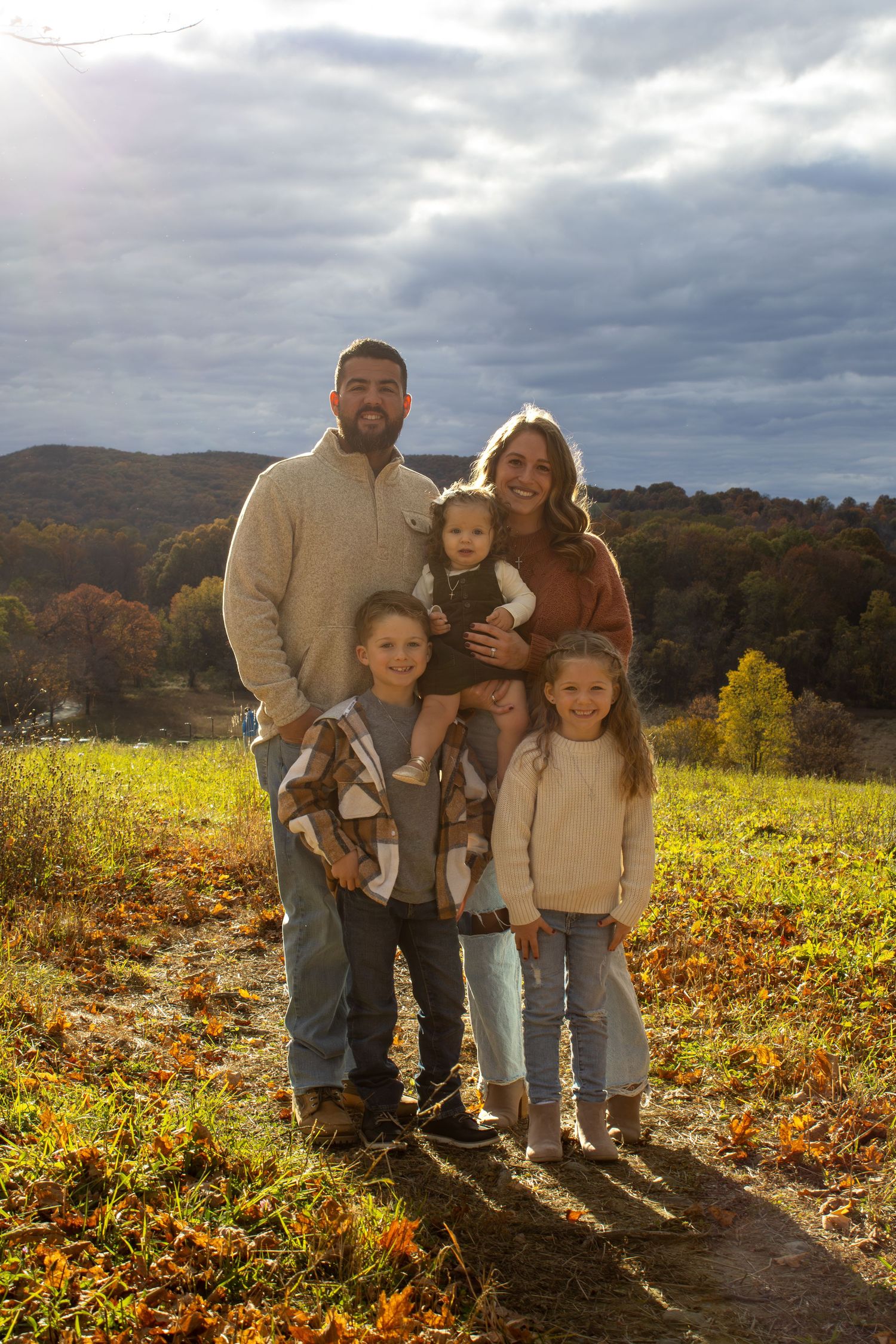 Family portrait on hillside with dramatic cloudy sky and autumn colors in background.